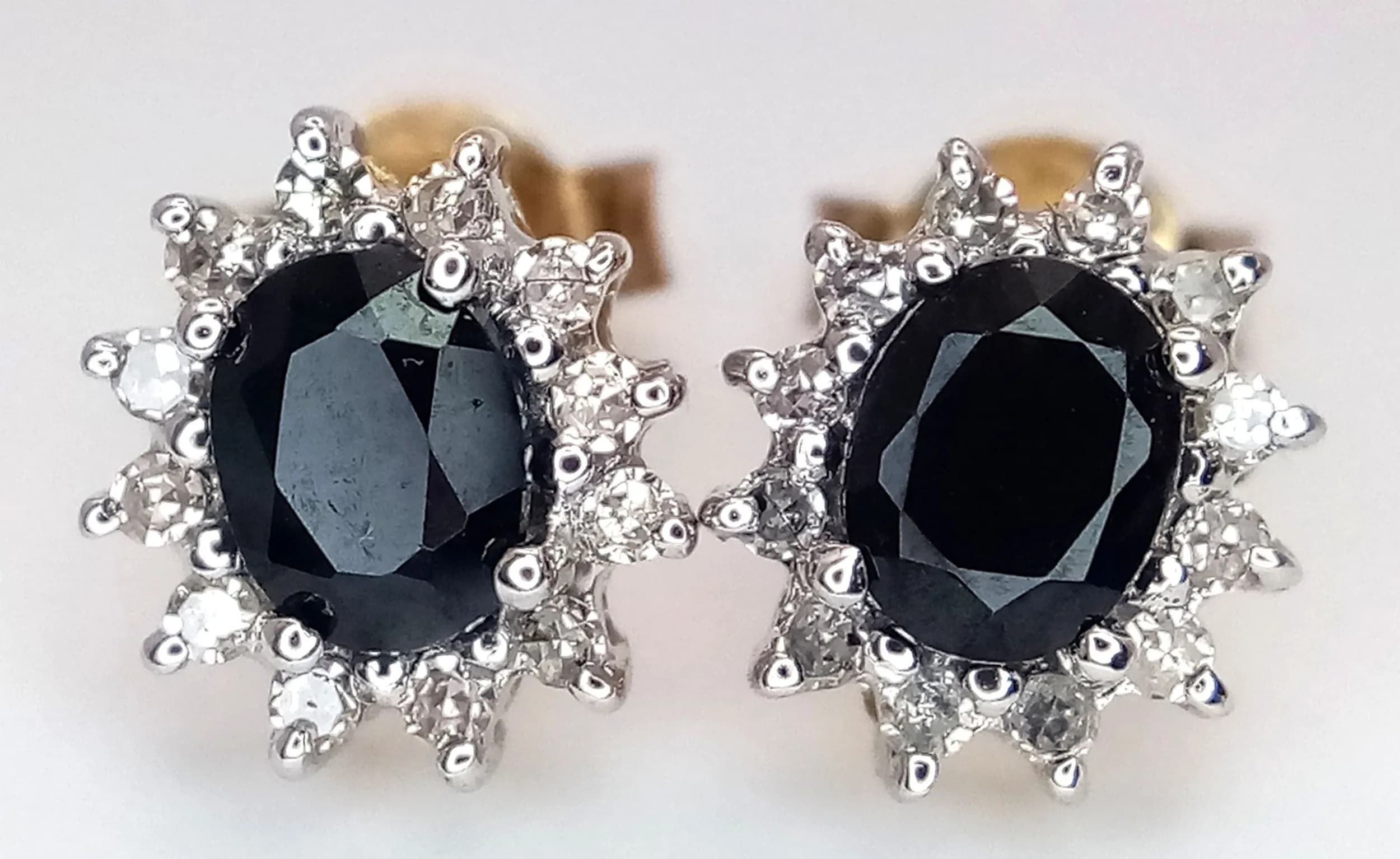A Pair of 9K Gold, Sapphire and Diamond Stud Earrings. Oval cut sapphire with diamond surround. 1.7g total weight.