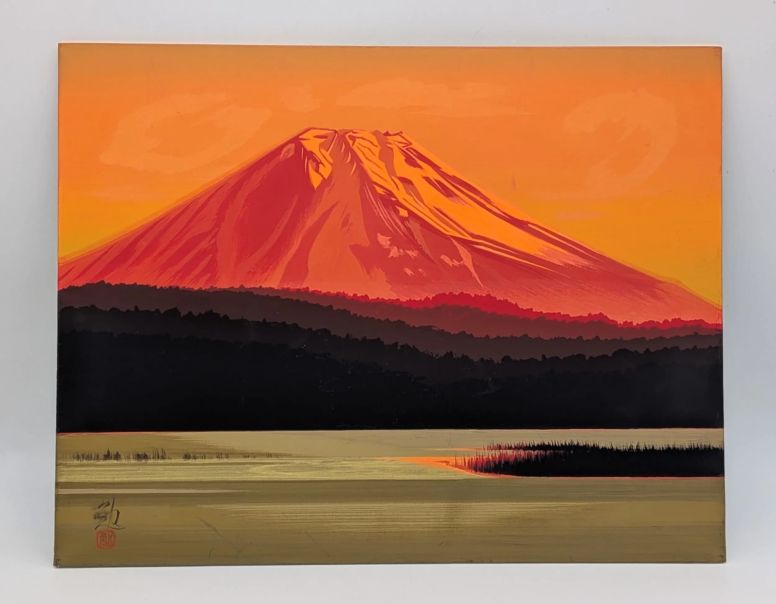 A Japanese Style Mount Fuji Landscape Painting. Depicting Mount Fuji in red and orange tones above a lake and forest landscape, with signature and red seal mark lower left. Height 32cm x Width 41cm.