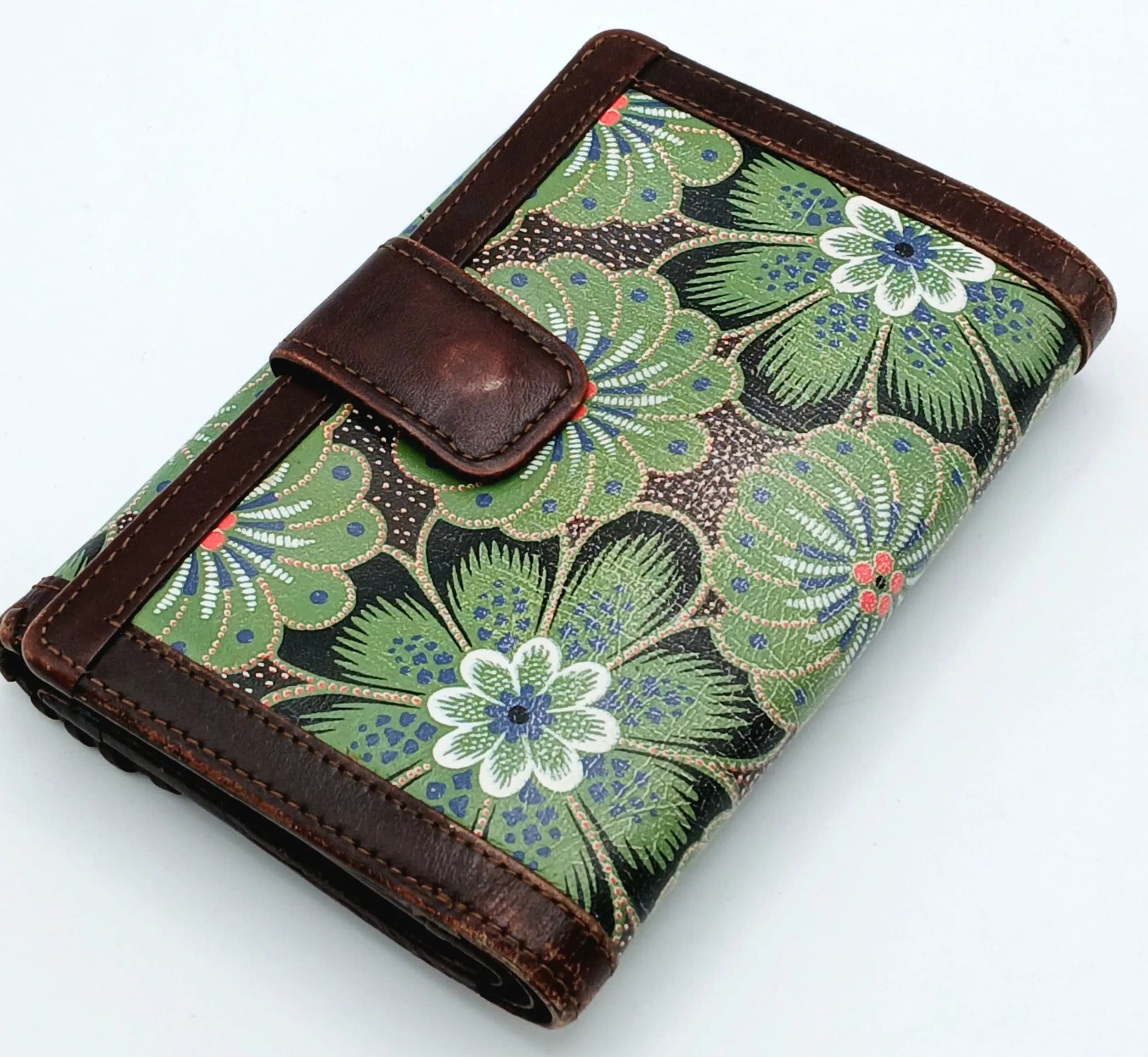 A Vivienne Westwood Floral Leather Wallet. Green floral printed leather exterior with dark brown leather trim and press-stud closure. Brown leather and green fabric interior with two main compartments. Features a section at the back with multiple card slots, note compartments, an ID window and a gusseted coin compartment. Approx. 14cm length x 10cm height (when closed). Some marks, signs of wear and tear to the leather. Please see photos or request a condition report. Ref: 29209.