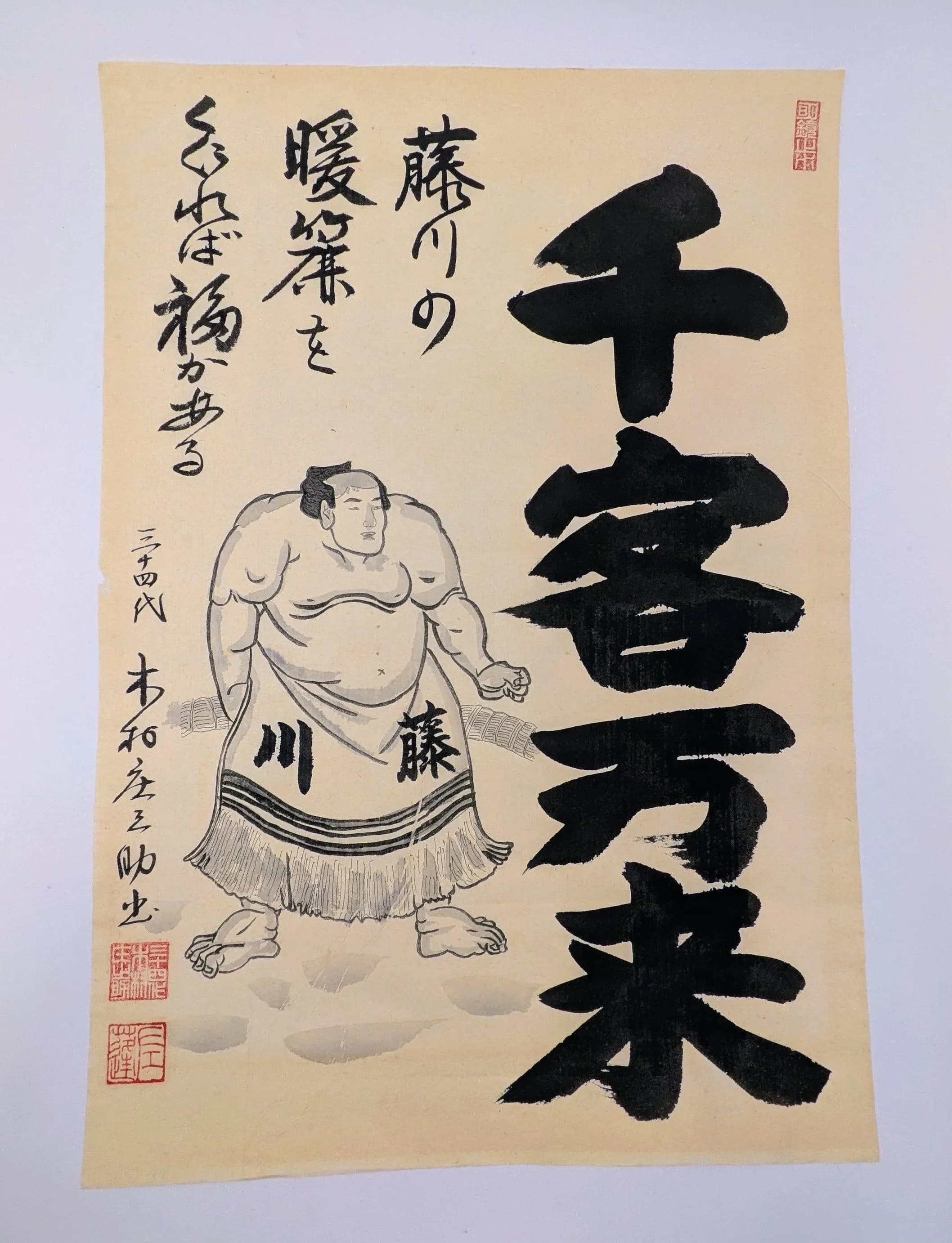 A Japanese Sumo Calligraphy Print. Depicting a sumo wrestler figure, bold black Japanese calligraphy and red seal marks. Approx 48.6cm height x 33.7cm width.