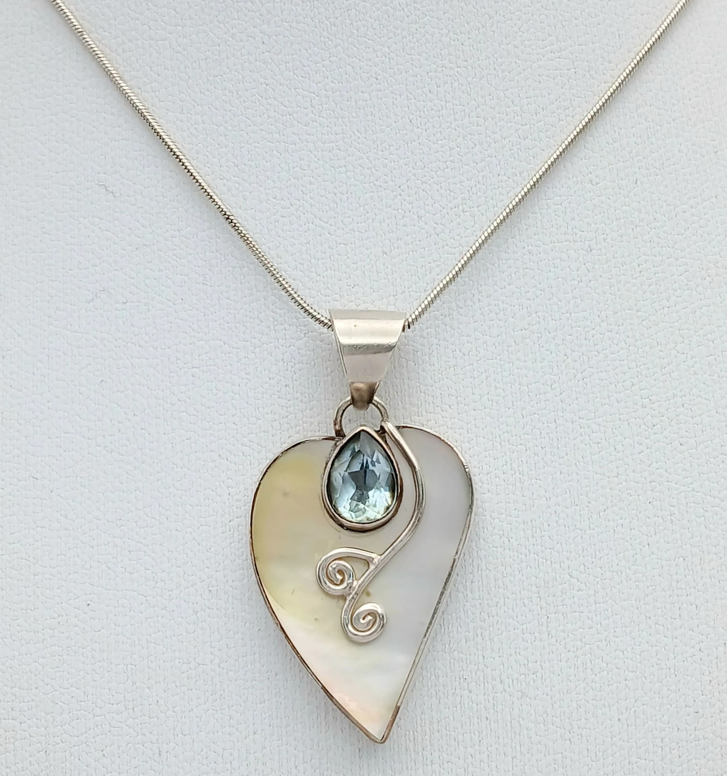 A Vintage Sterling Silver Blue Topaz and Mother of Pearl Heart Pendant Necklace- 41cm Length Rope Chain. The Pendant measures a 3.5cm drop, 2cm width. Set with a 7 x 6mm Tear Drop Cut Blue Topaz, approximately 1 Carat, on a Mother-of-Pearl Background. Gross Weight 9.15 grams.