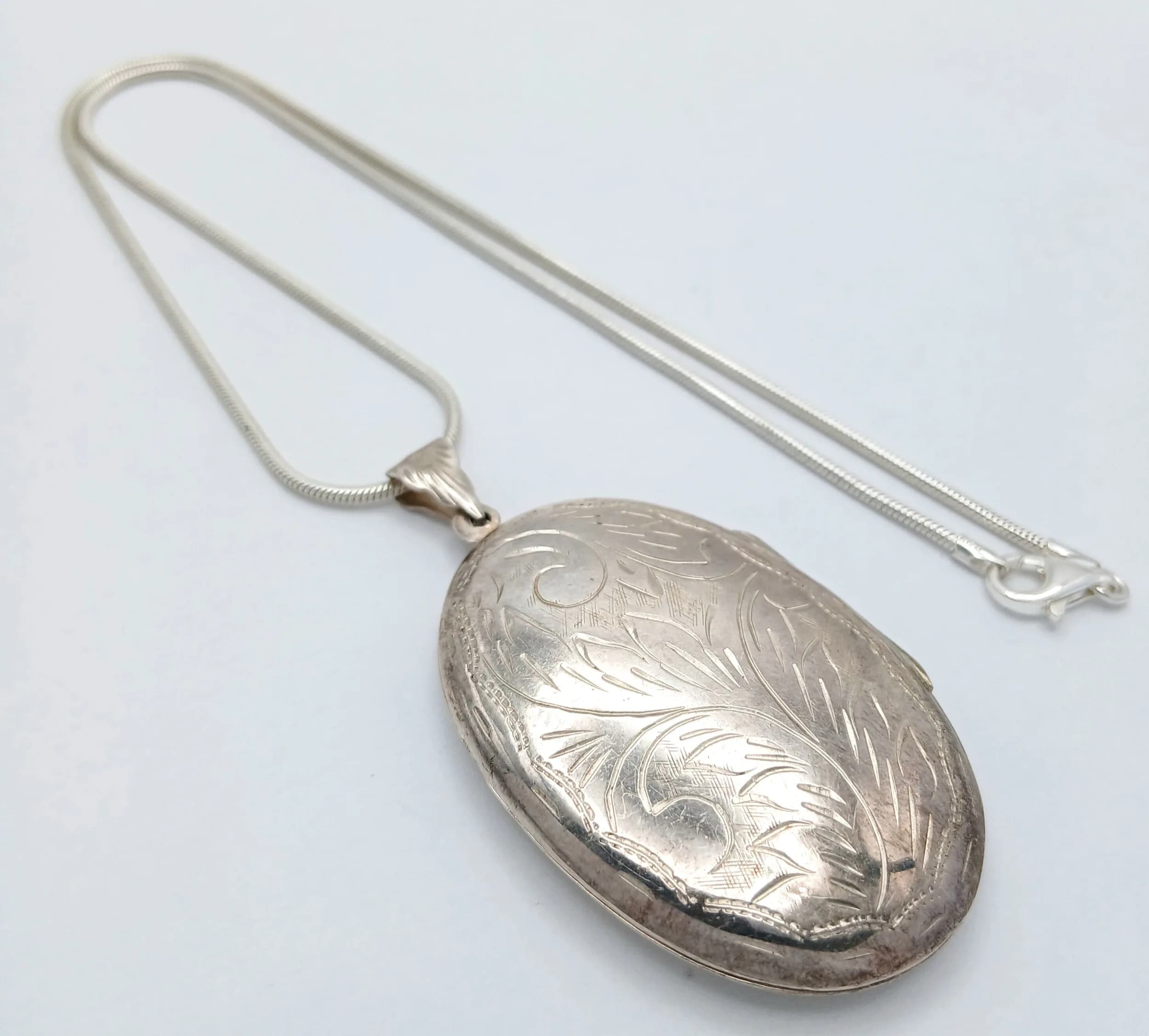 A 925 Silver Oval Locket Pendant Necklace. The locket features engraved foliate decoration, 6cm length. 41.5cm length necklace. 19.77g total weight.