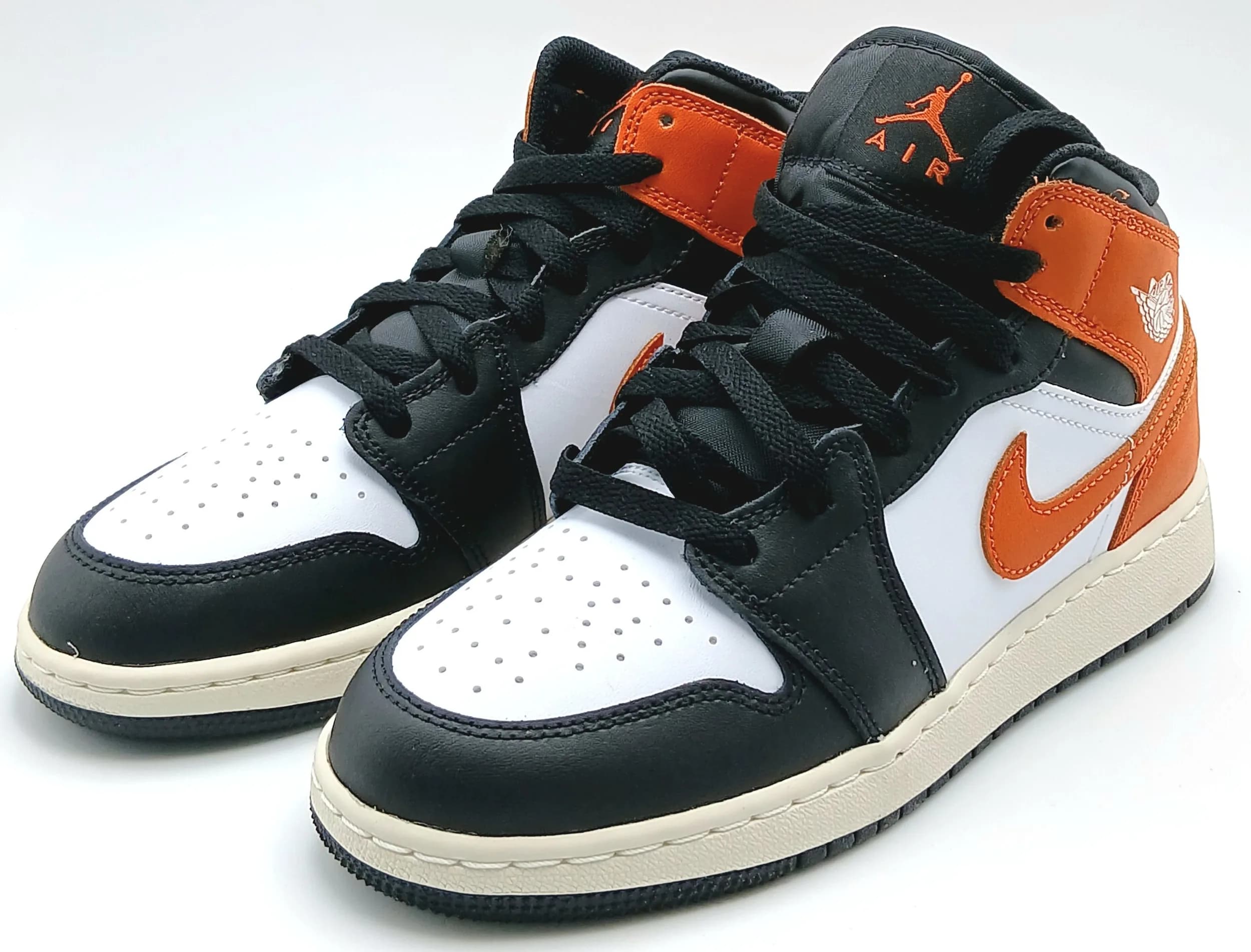 A pair of Nike Air Jordan 1 mid trainers in white, orange and black leather. New, no box. UK size 5, US size 5.5Y
