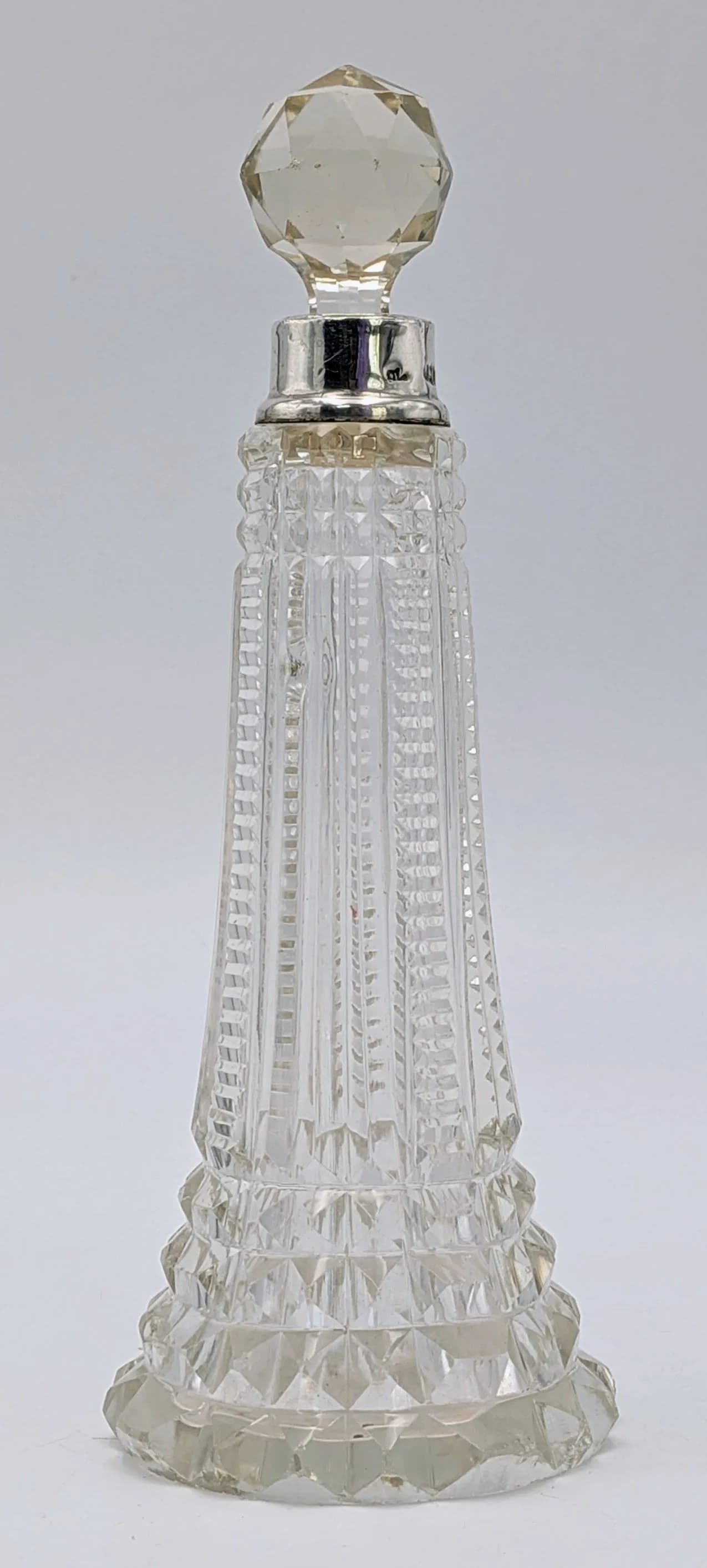 An Antique Cut-Glass Scent Bottle with an Elegant Panel-Cut Body and Multi-Faceted Crystal Stopper. Sterling Silver Collar. Hallmarks for London 1913. 18cm height.