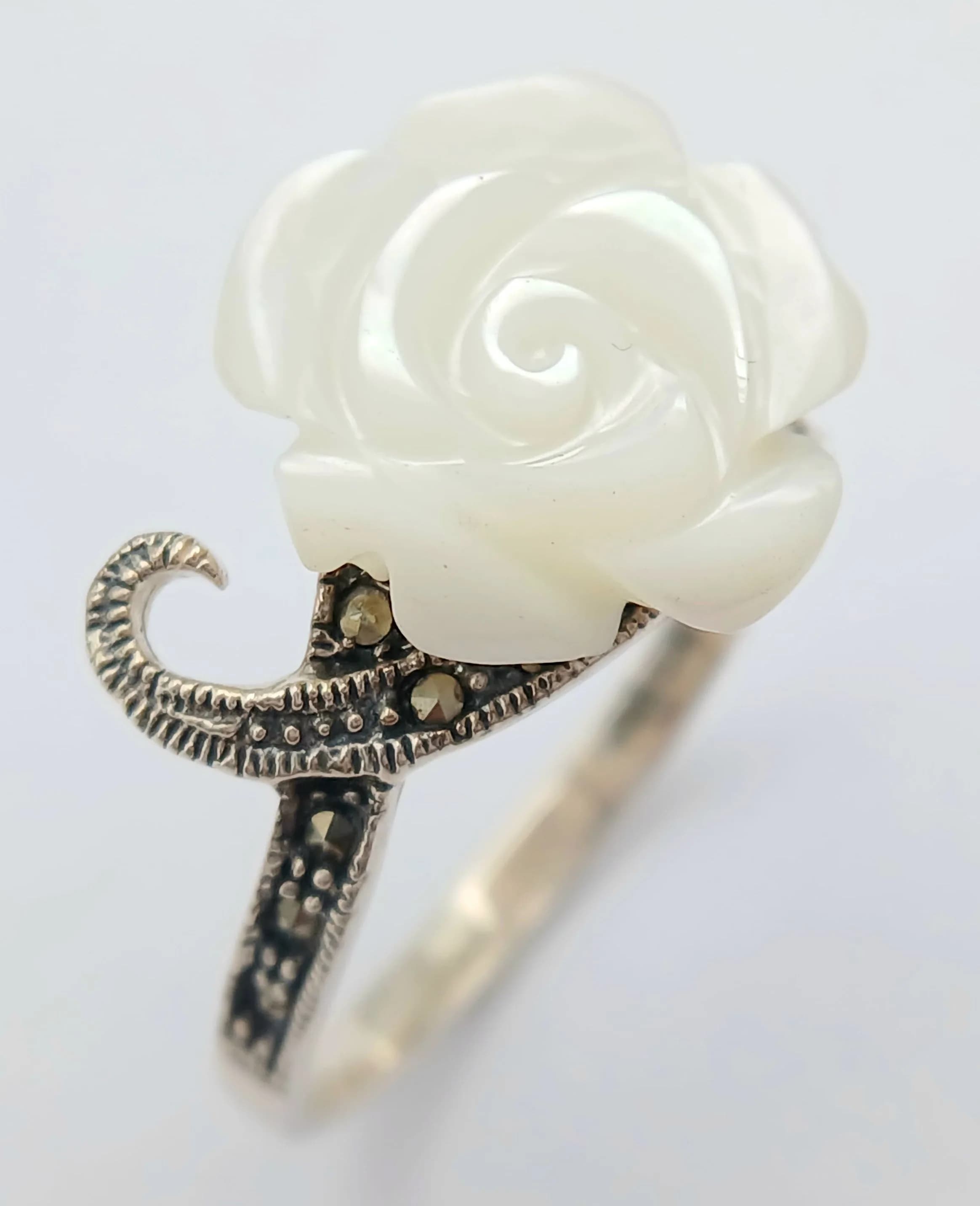A Vintage and Unique Sterling Silver Rose Carved Mother of Pearl and Marcasite Ring Size W1/2. The Ring is intricately detailed with the Rose measuring 1.6cm Diameter. Gross Weight 3.45 grams.