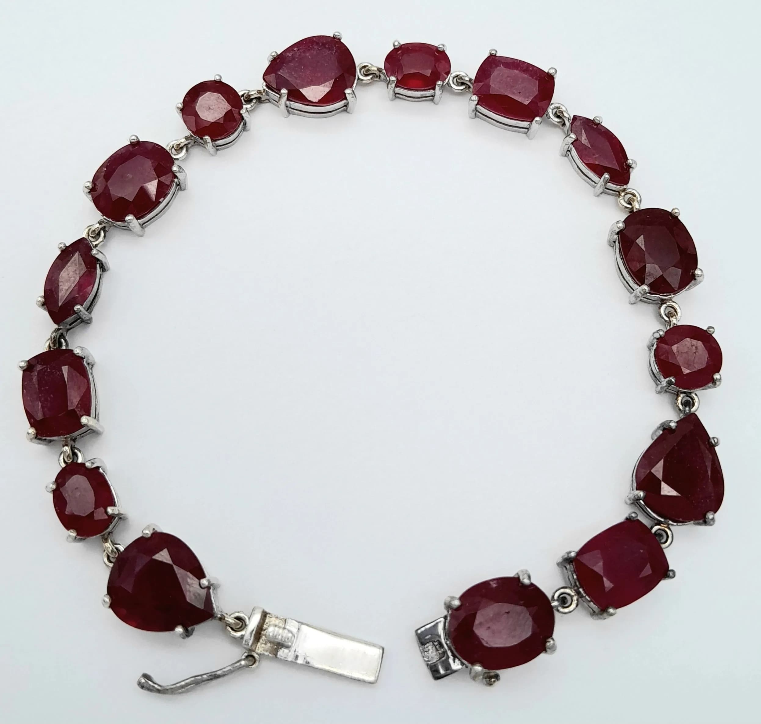 A Wonderful Sterling Silver Multi-Cut Glass Filled Ruby Set Tennis Bracelet- 19.5cm Length. Set with Oval, Rectangle, Marquise and Tear Drop Cut Rubies. 8mm width and widest point. Gross weight 19.49 Grams.