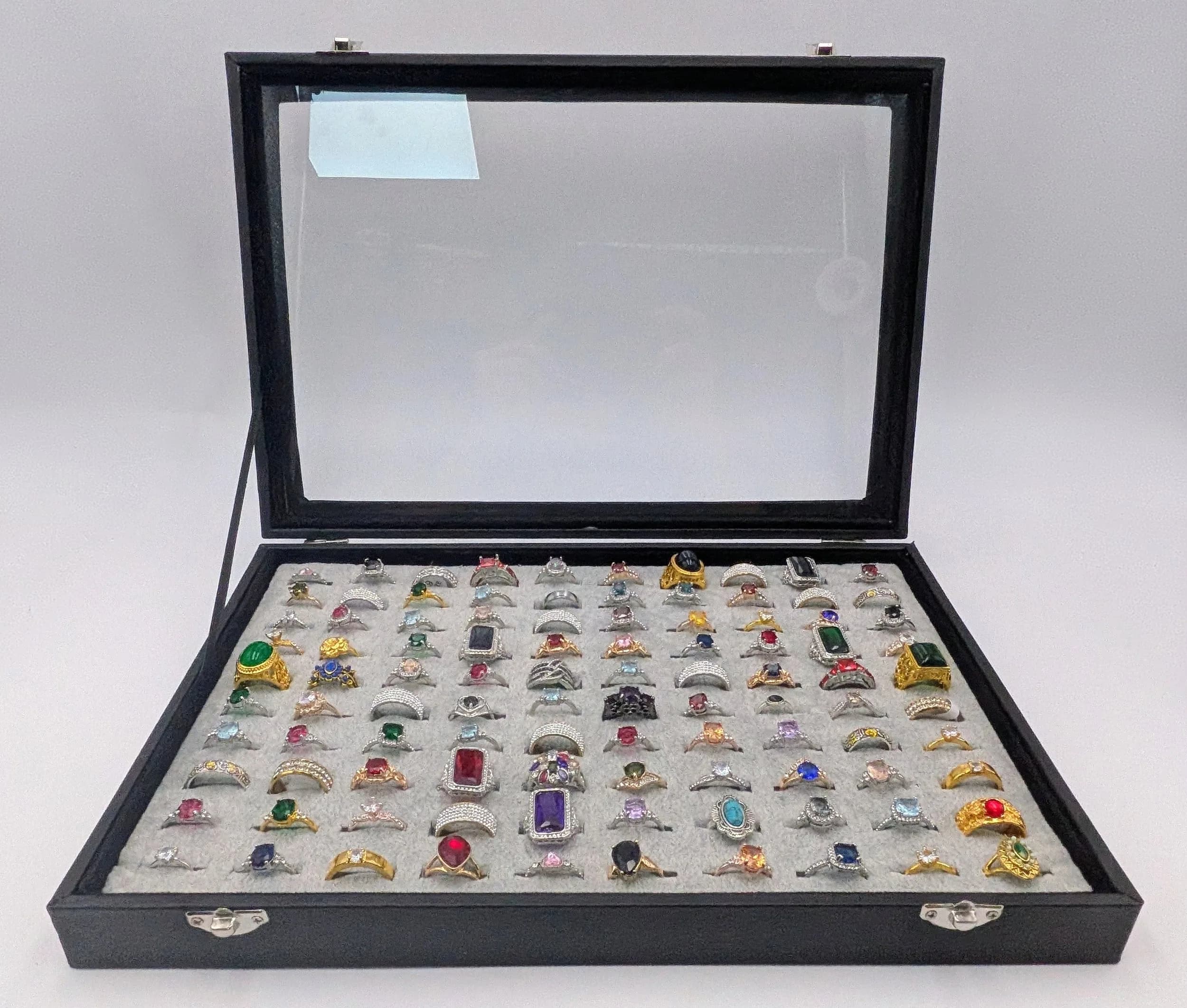 A Jewellery Display Case with 100 Rings! An absolutely fabulous lot with different colored stones to acrylic/resin decoration. All types of stone cuts with gilded and white metal shanks of different design. Sizes range from small to large. All rings in excellent condition. Case size - 35 x 24cm.