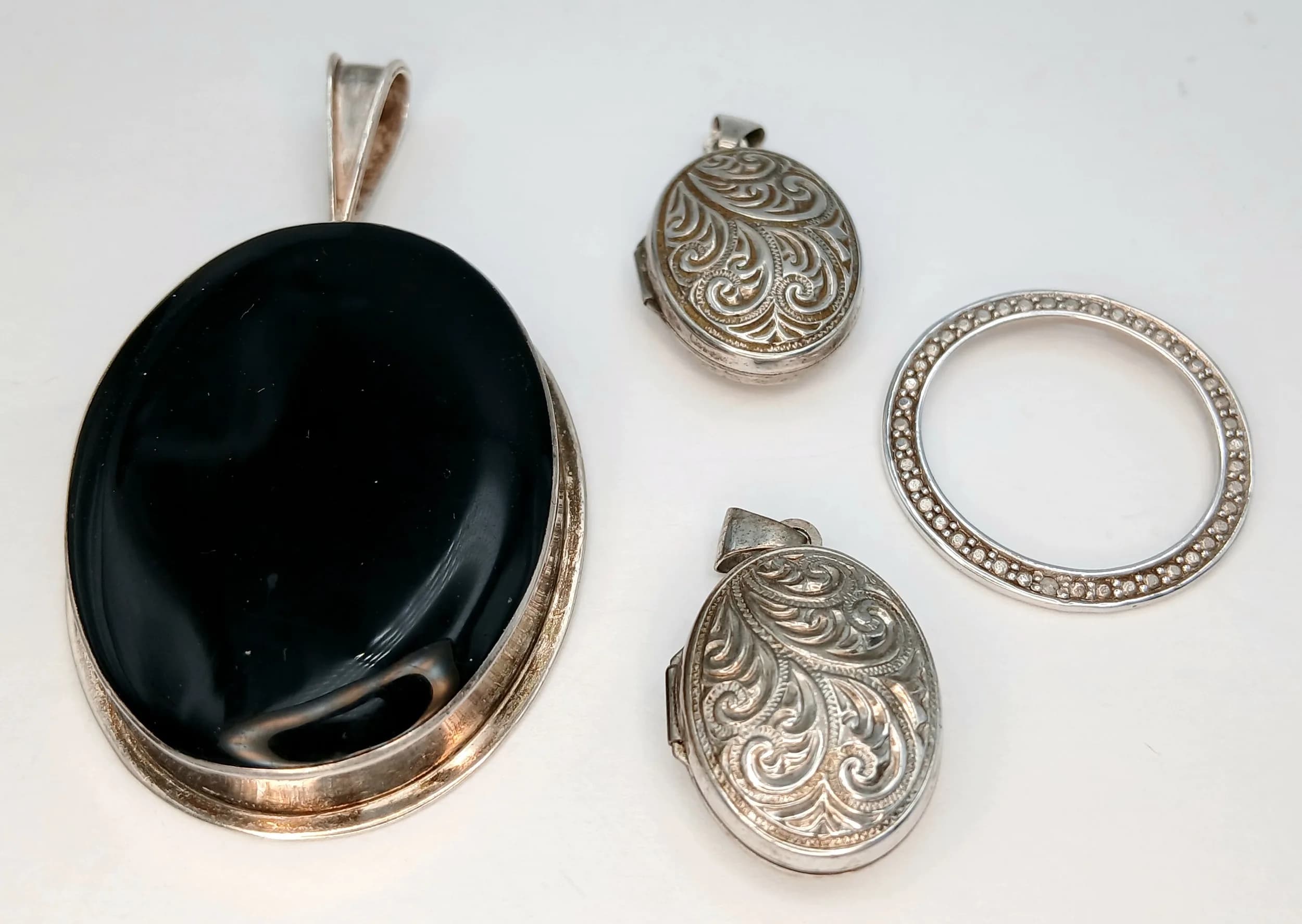 Four Silver Pendants. Comprising a pair of oval engraved locket pendants, a circular openwork pendant and a large oval black onyx pendant. 33.40g total weight.
