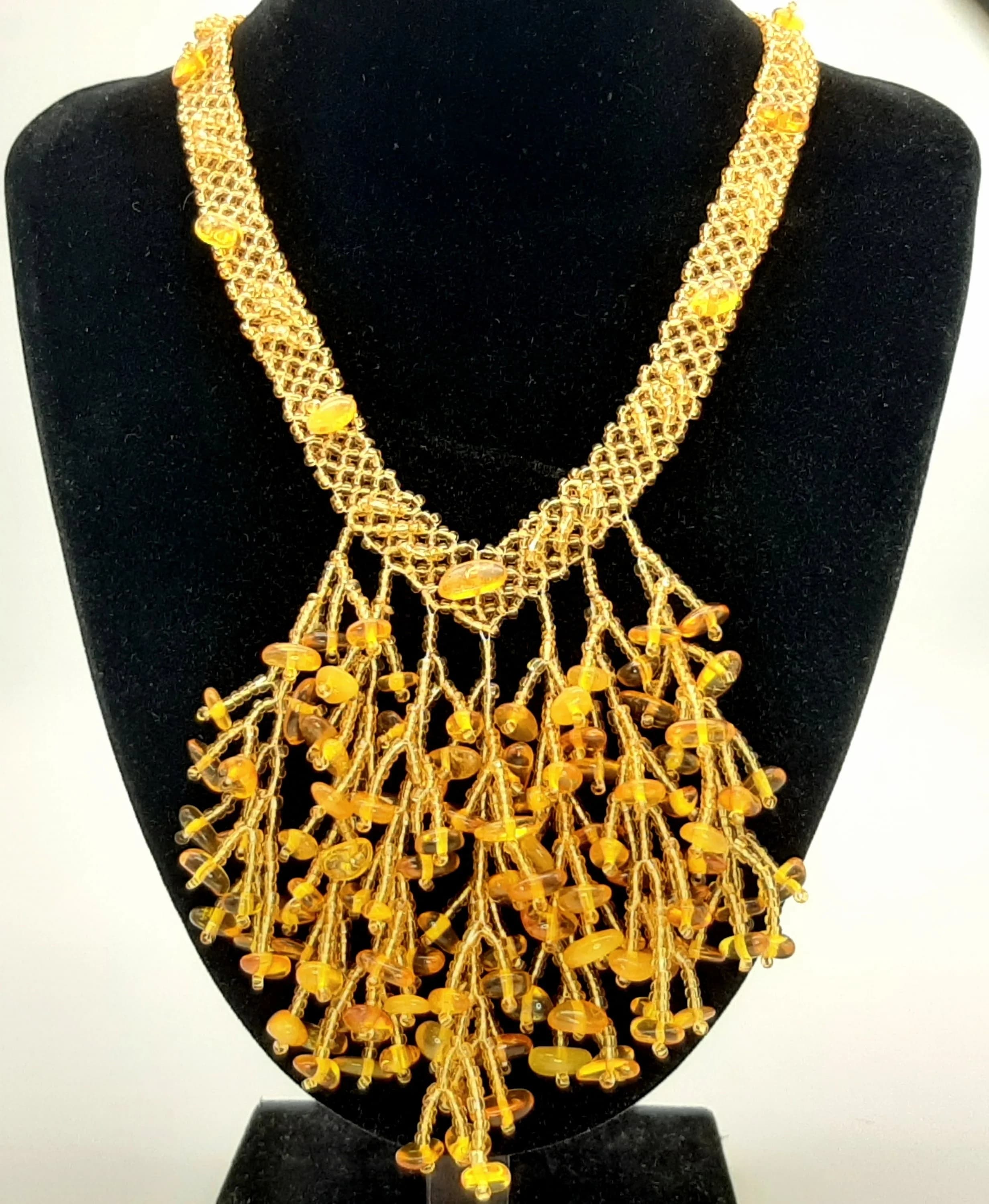 A Striking Baltic Amber Bead Necklace. Measuring 43cm in length with an 8cm drop. Features a woven gold-tone bead collar suspending cascading strands set with polished Baltic amber beads in honey and cognac tones. Handmade in Russia.