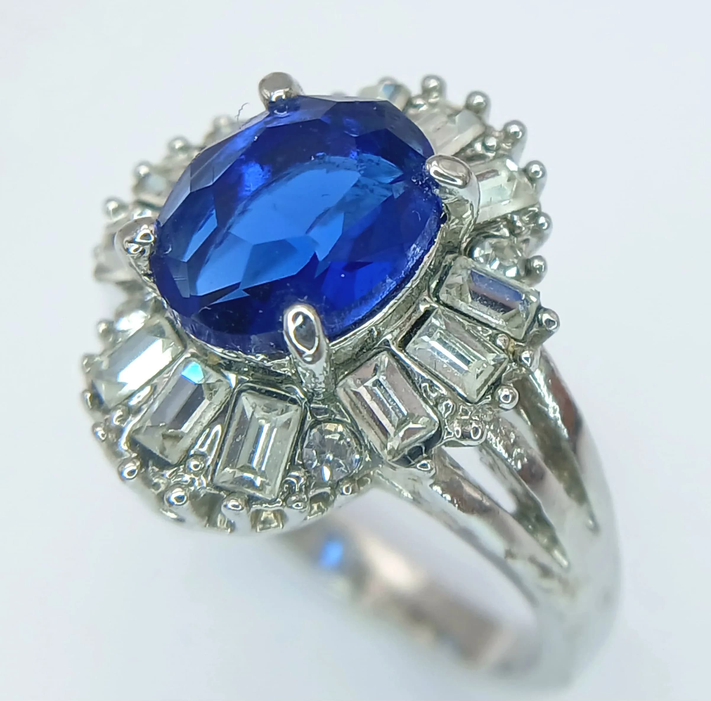 An Impressive Art Deco Design Unmarked White Metal, Sapphire Blue and White Stone Cluster Ring Size S. The Crown measures 1.8 x 1.6cm. Gross Weight 8.96 grams