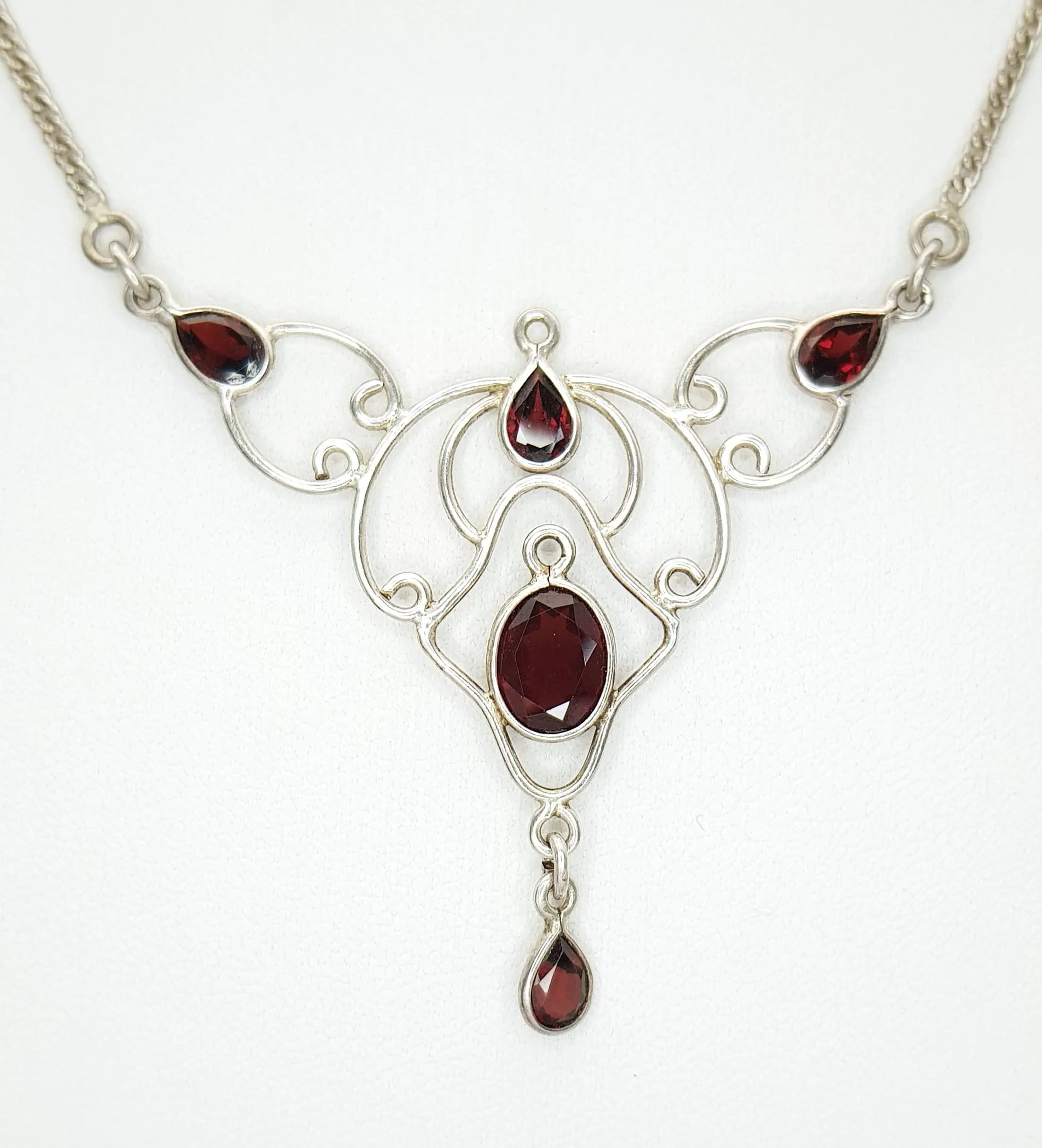 An Attractive 925 Sterling Silver Garnet Pendant Necklace - 40cm Length. Features an ornate pendant set with oval and pear cut garnets in an openwork silver design on a fine curb link chain. The pendant measures 5cm x 4.5cm. Gross weight 6.93 grams.