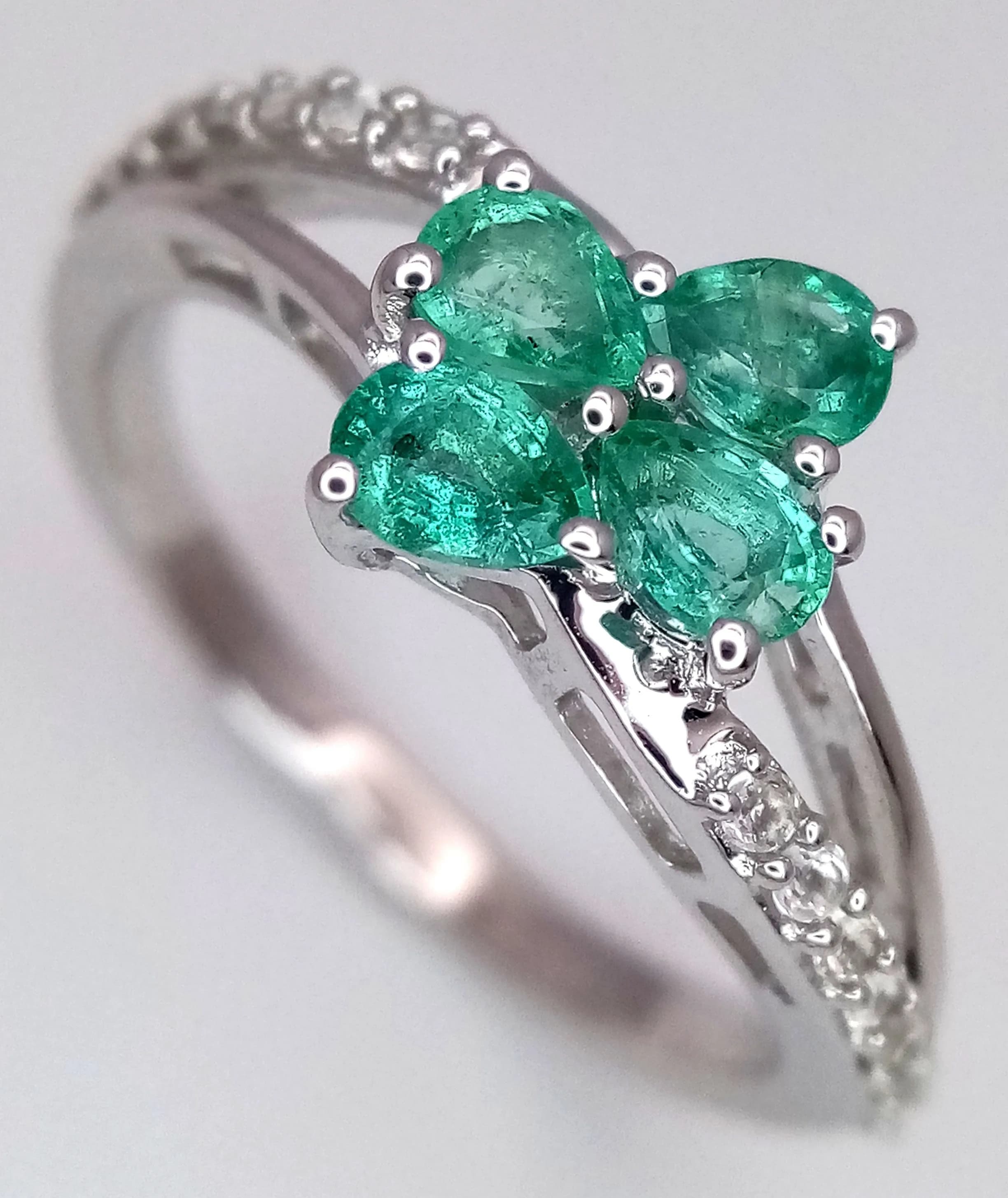 A Pretty Sterling Silver Emerald and White Spinel Ring. Size O. The Ring is set with Four 4 x 3mm Pear Cut Emeralds that total approximately 0.80 carat and with round cut White Spinel in the upper shank. The Ring has a grossweight of 2.16 grams.