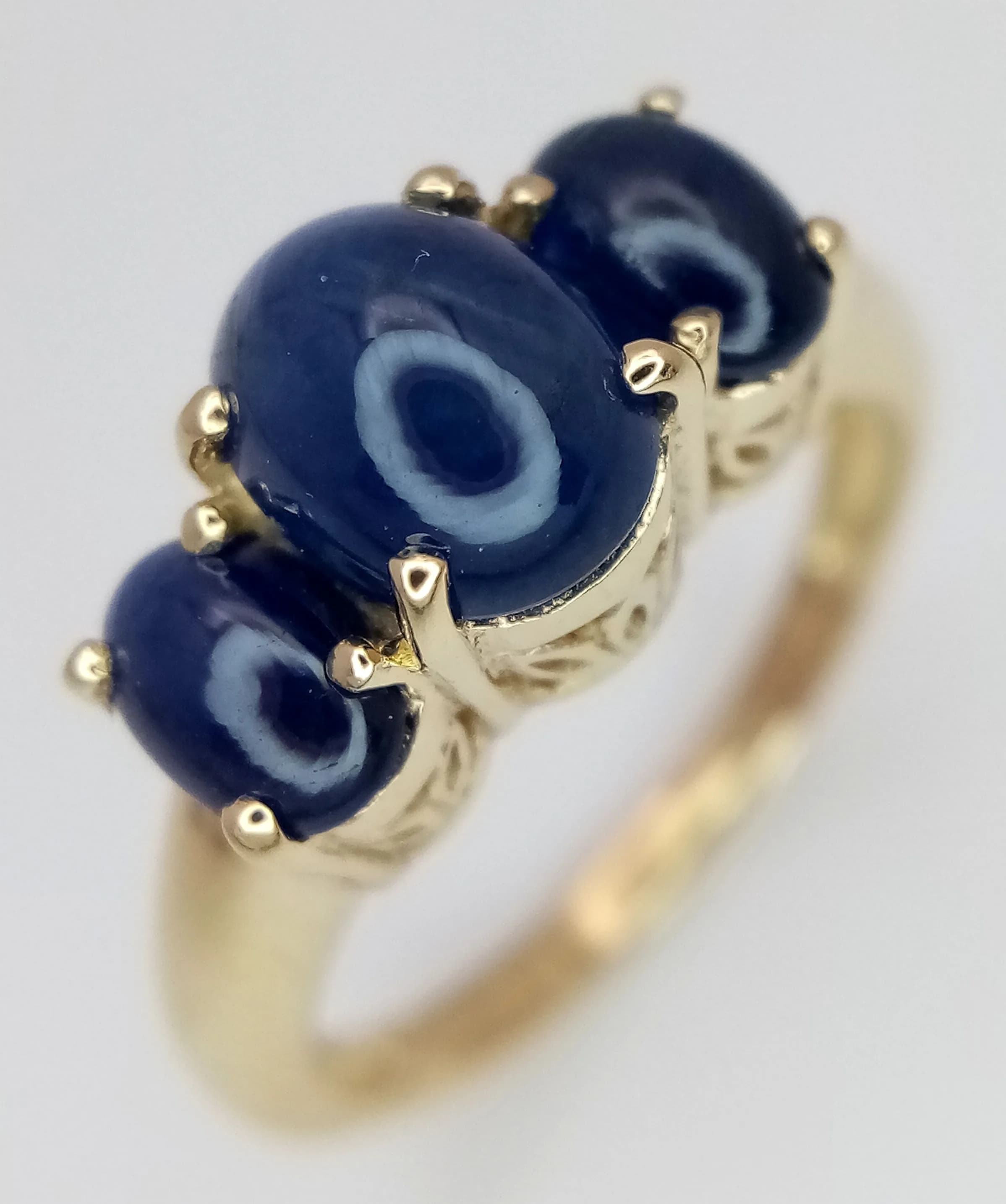 An Exception 9k Yellow Gold Blue Sapphire Cabochon Trilogy Ring-Size N. The Ring is set with three Oval Cut Blue Sapphire Cabochons, the centre measuring 8 x 6mm, 1.27 carat, and two 6 x 4mm of 0.44 carat each, total 2.15 ctw. The Ring has a gross weight of 3.56 grams. Appears practically unworn if worn at all.