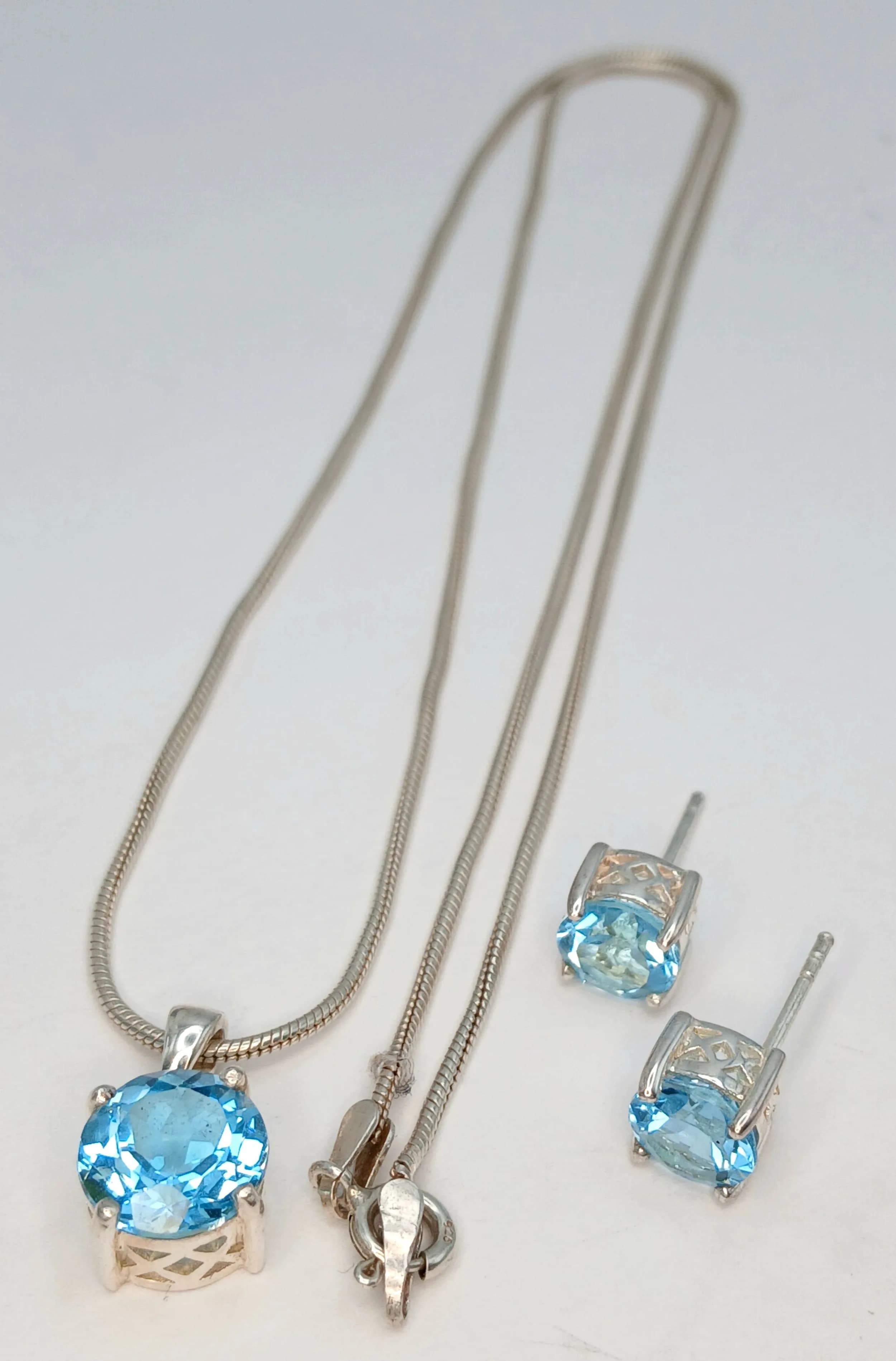 A 925 Silver Blue Topaz Pendant Necklace and Matching Stud Earrings. All set with round cut blue topaz stones. 49cm length necklace. 8.88g total weight.