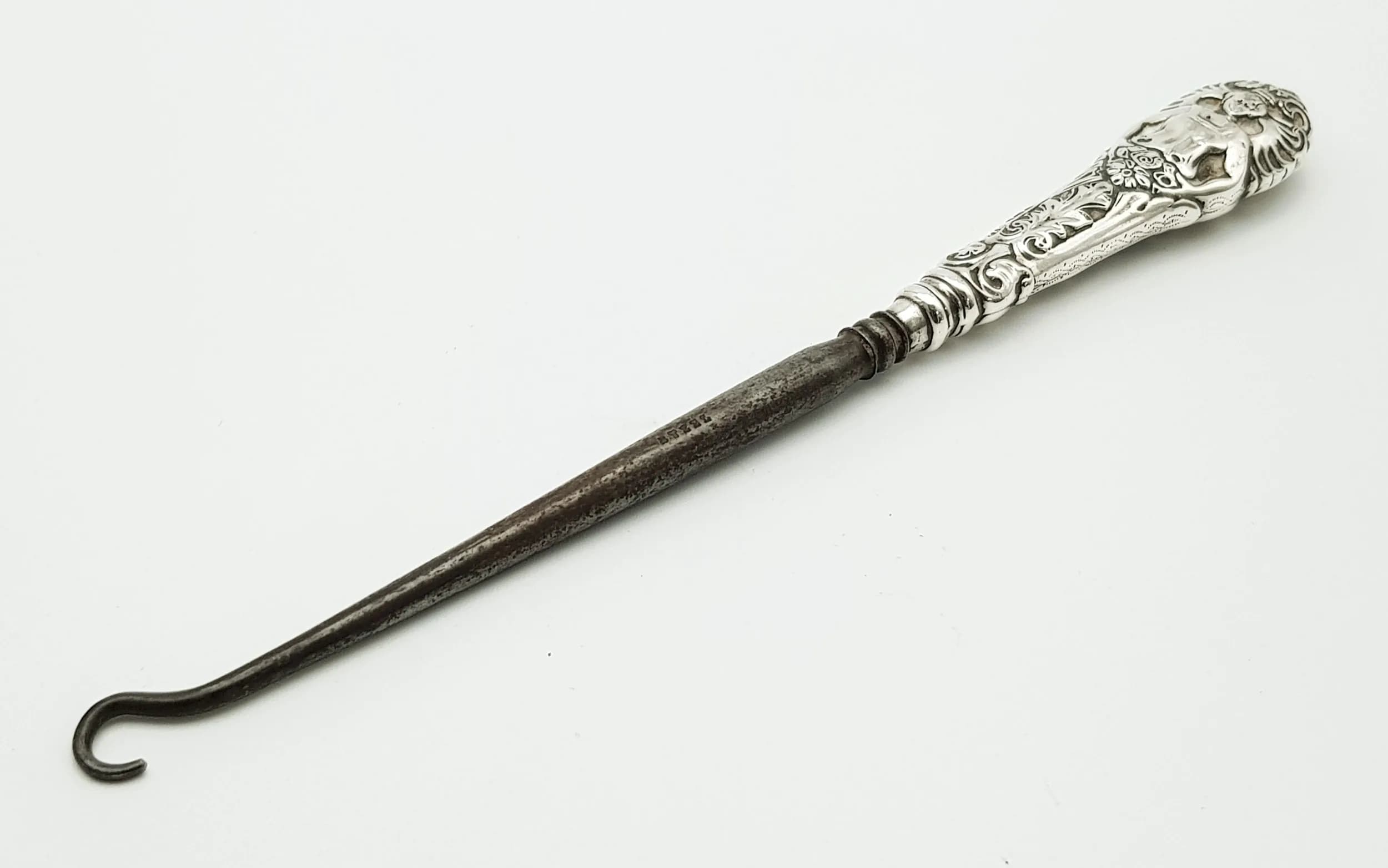 An Antique Silver Handled Crochet Hook. 1900 Birmingham hallmarked. Features silver handle with embossed floral and scroll decoration, fitted with a steel crochet hook. Measures approx 17.5cm length. Total weight 30.74 grams.