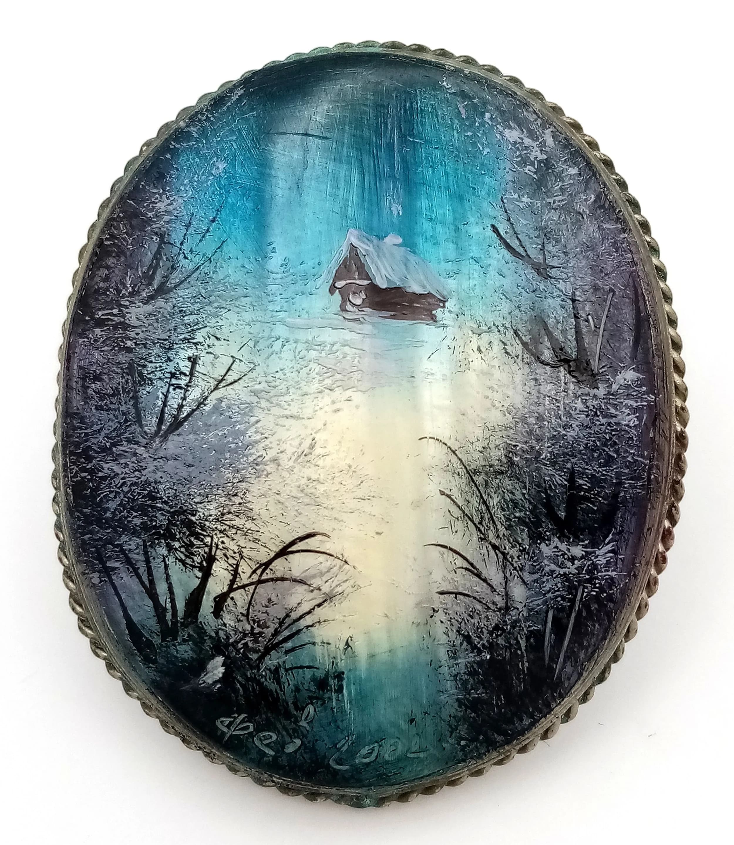 A Hand-Painted Mother of Pearl “Winter Scene” Brooch. Measuring approximately 5cm. Features an oval mother of pearl panel depicting a snowy landscape with a cabin and trees in iridescent blue and white tones, within a decorative mount. Handmade in Russia.