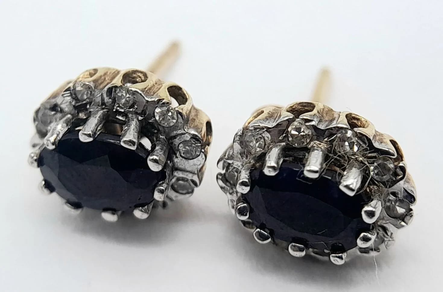 A Beautiful Pair of 9k Yellow Gold Blue Sapphire and Diamond Stud Earrings. 9 x 6mm. The Earrings are set with 6 x 4mm Oval Cut Blue Sapphires, circa 0.50 carat each and with Ten round cut diamonds in each, approximately 0.05 carat total in each earring. Combined Gross weight of theearrings is 1.67 grams.