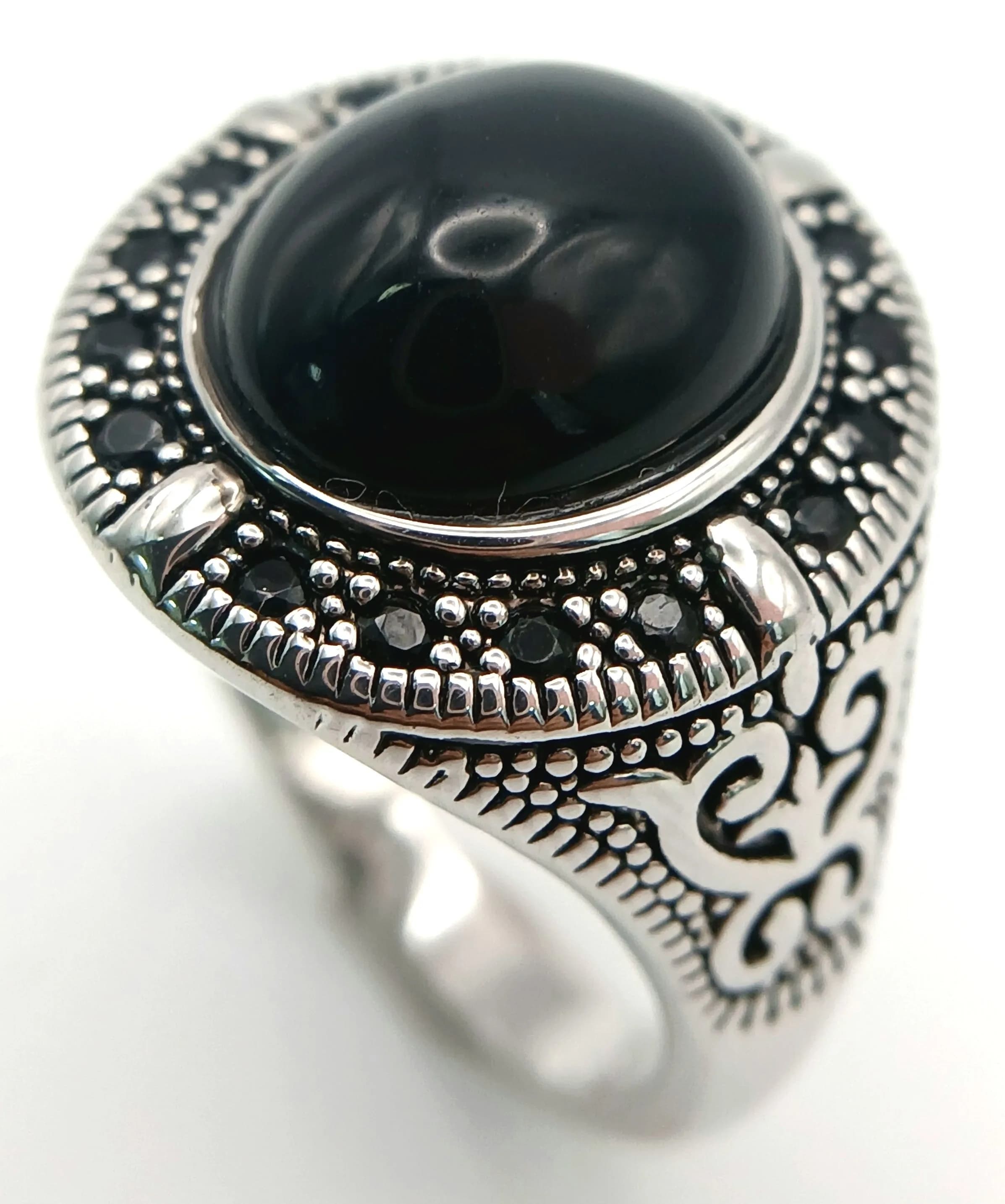 A Beautiful 925 Silver Black Onyx Cabochon Ring. Size Q. Features an oval black onyx cabochon framed by onyx detailing in a decorative silver setting. The centre onyx measures 1.2cm x 1cm. Gross weight 5.77 grams.