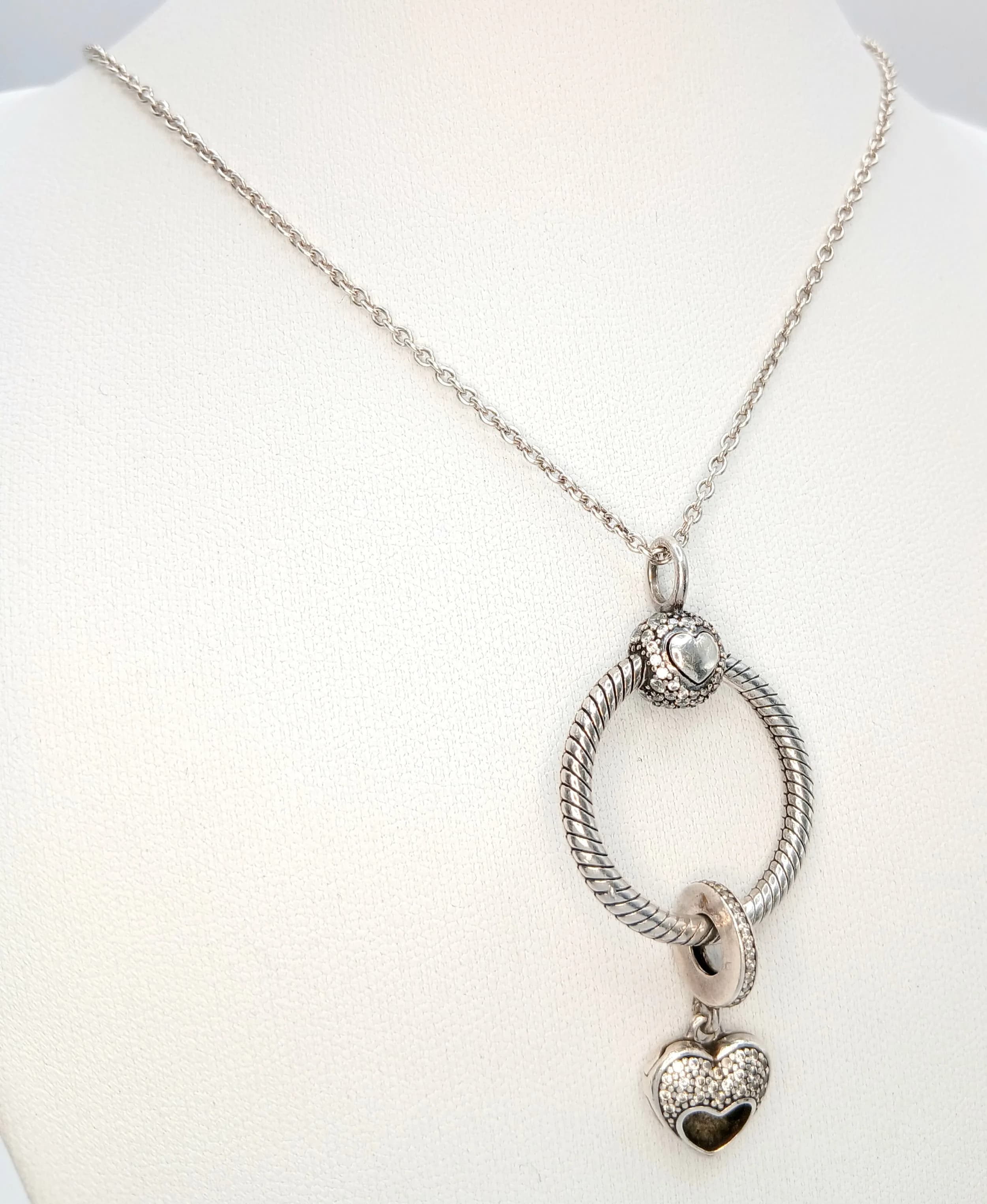 A Pandora 925 Silver Necklace with an Openable Heart Pendant. Heart pendant engraved “I Love My Mom” with stone set detail. Total weight 15.88g. Approx 90cm chain length with a 4cm pendant drop. Comes with Pandora box.