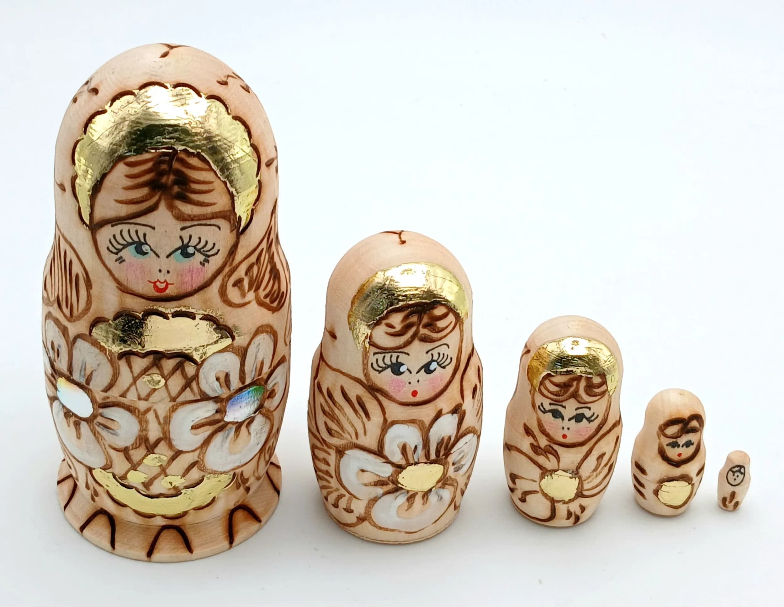 A Traditional Russian Nesting Doll Set. Five-piece wood burned wooden nesting doll set featuring a floral design with natural finish and gilt highlights. Handmade in Russia. Tallest doll measures approximately 11cm. All dolls fit inside each other.