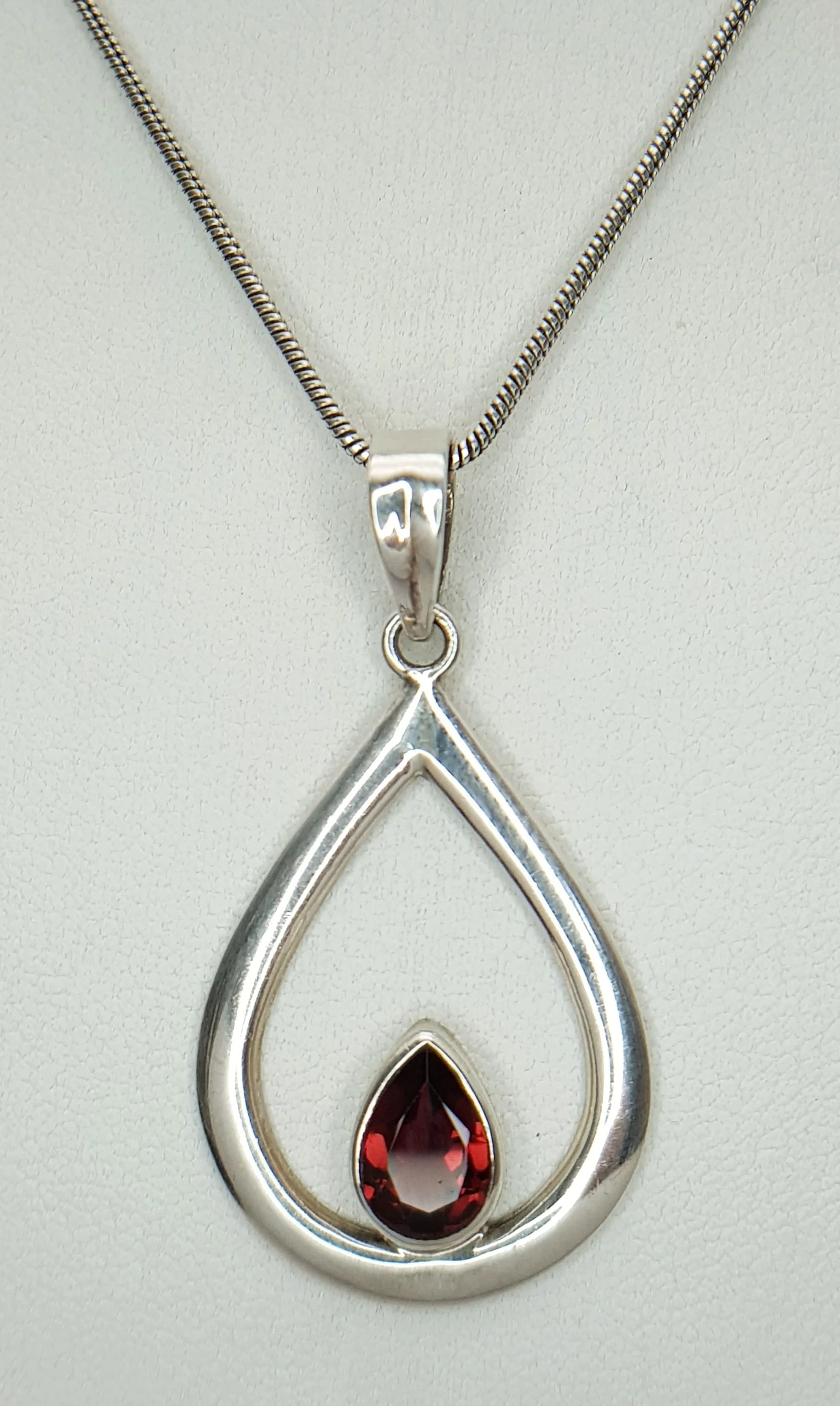 A Pretty 925 Sterling Silver Garnet Pendant Necklace - 51cm Length. Features a pear cut garnet suspended within an open teardrop design on a fine snake chain. The pendant measures 3cm x 2cm. Gross weight 7.76 grams.