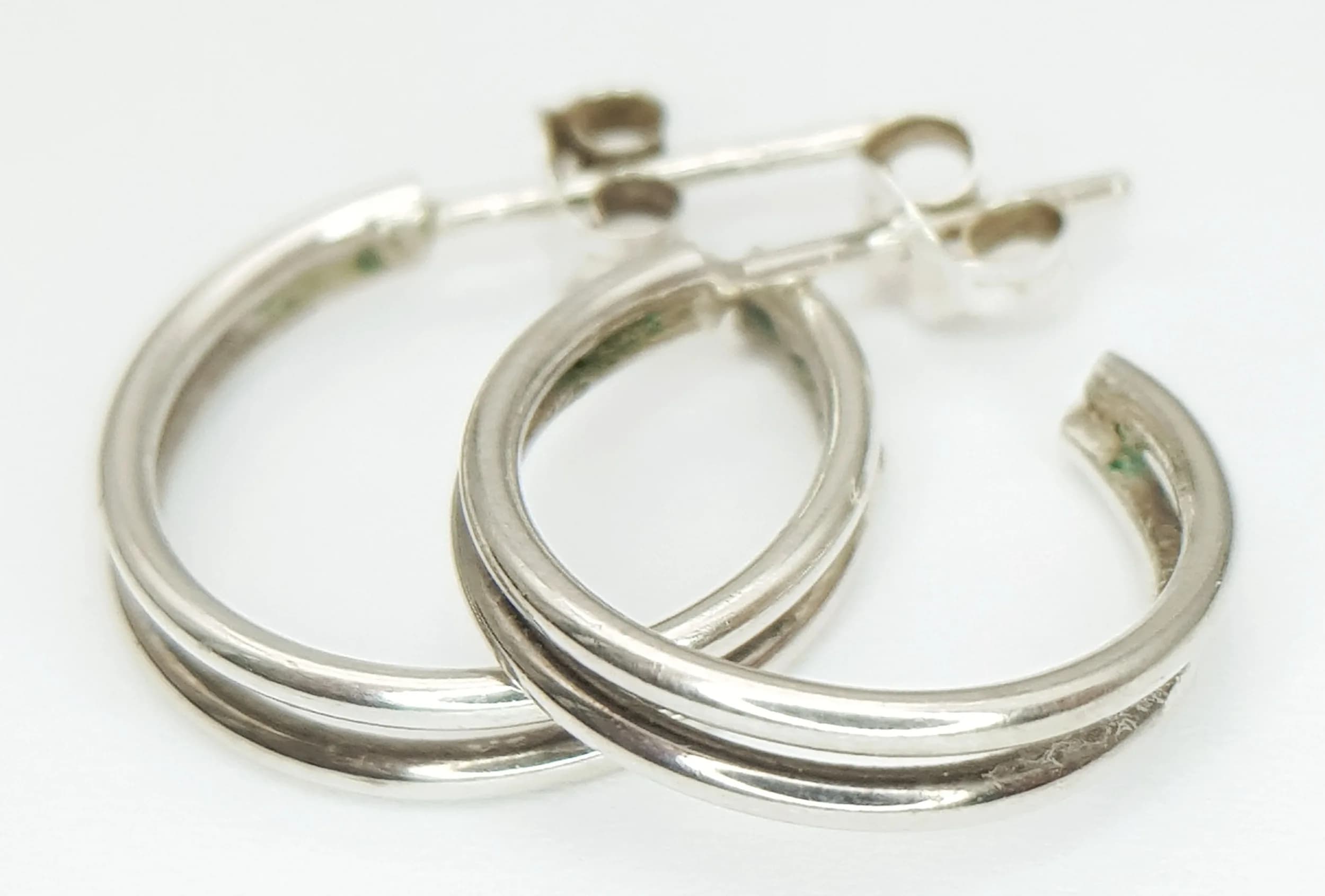 A Stylish Pair of 925 Sterling Silver Double Hoop Earrings. Features a polished overlapping double hoop design with post and butterfly fittings. Each earring measures 1.5cm diameter. Gross weight 2.54 grams.