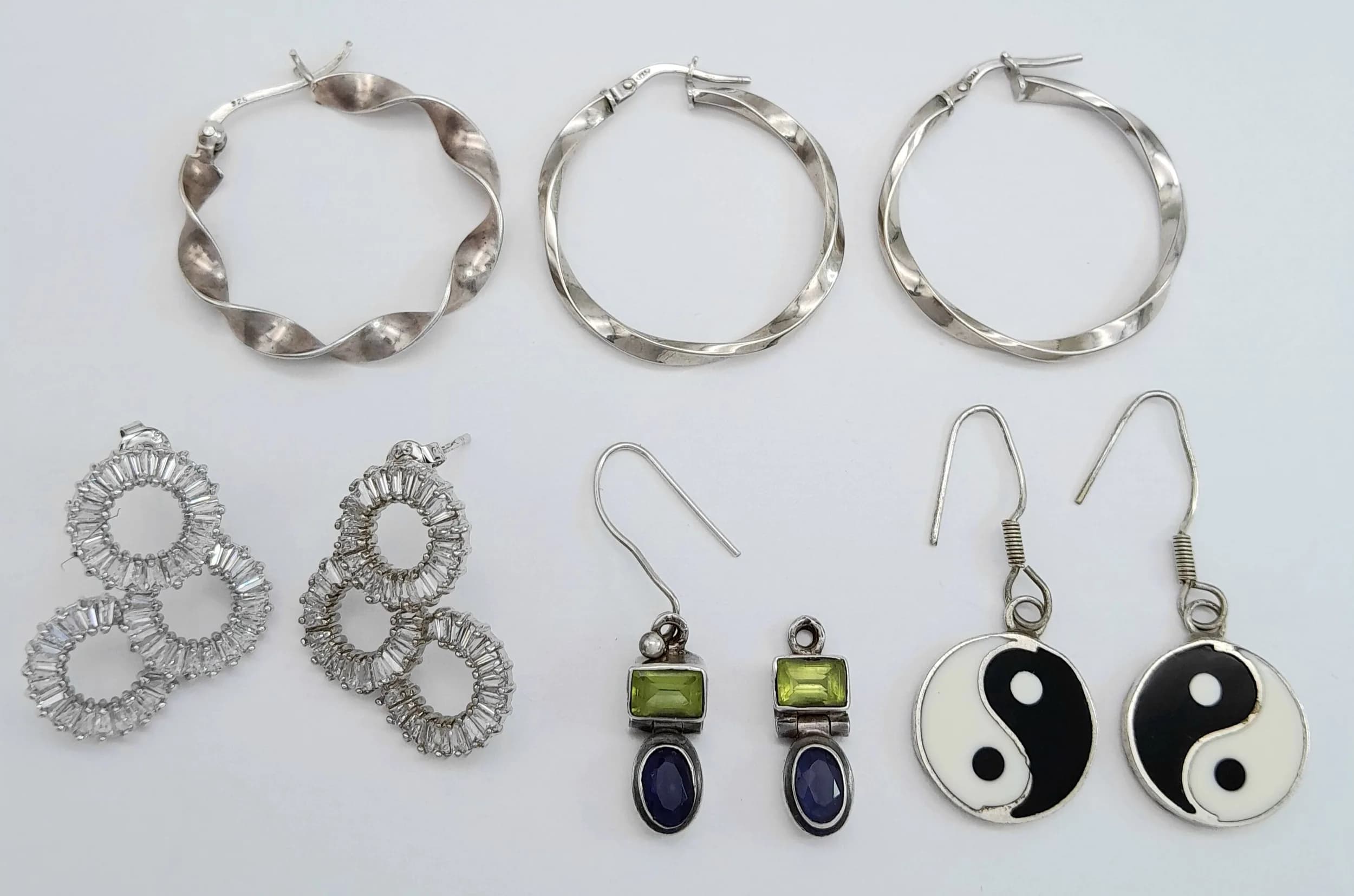 A Group of Sterling Silver Earrings. Comprising a pair of textured circular cluster stud earrings, a pair of hoop earrings, a pair of drop earrings set with green and blue gemstones (one missing earring hook), a pair of black and white yin-yang drop earrings, and a single twisted hoop earring. All stamped or hallmarked 925 and Yin-Yang Earrings marked Mexico Alpaca. Total weight 16.25gms.