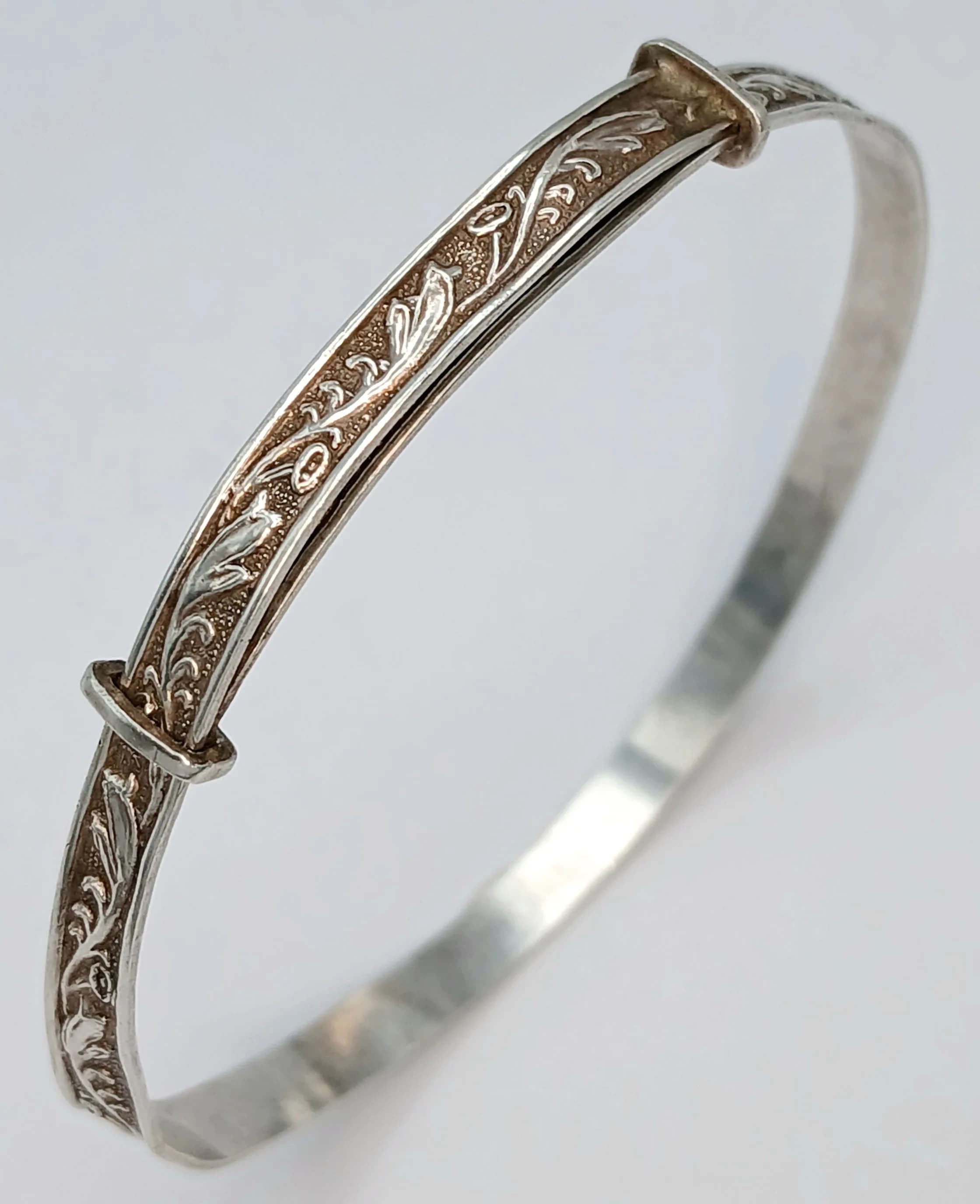 A Vintage Silver Adjustable Engraved Bangle - 6cm Diameter. Features an engraved scrolling foliate design to the front with an adjustable hinged band. The band measures 0.5cm wide. Gross weight 5.06 grams.