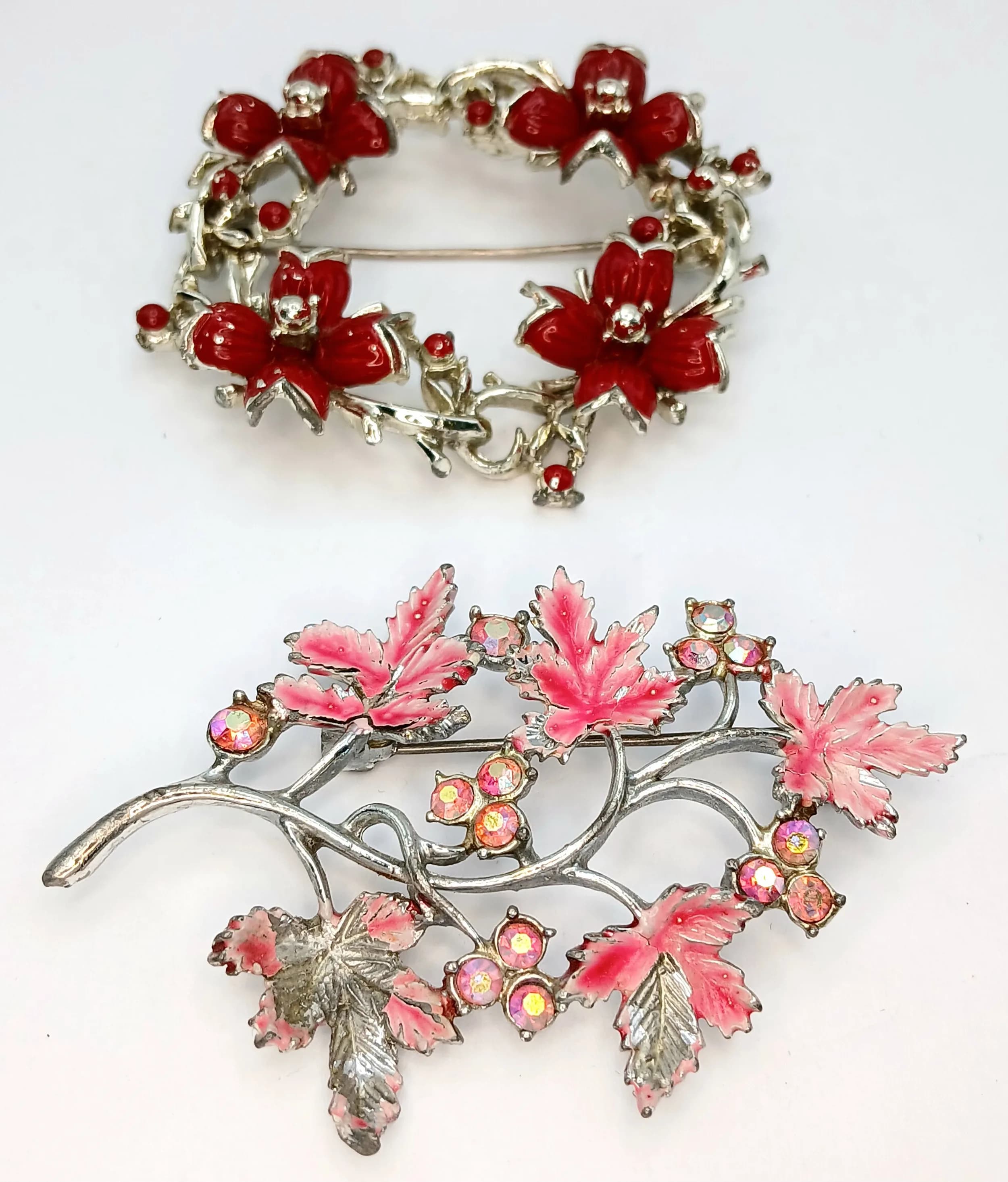 Two Gold-Tone Enamel Floral Brooches. Comprising a red enamel floral wreath brooch, approx 6cm diameter, and a pink enamel floral brooch set with iridescent stones, approx 7cm length.