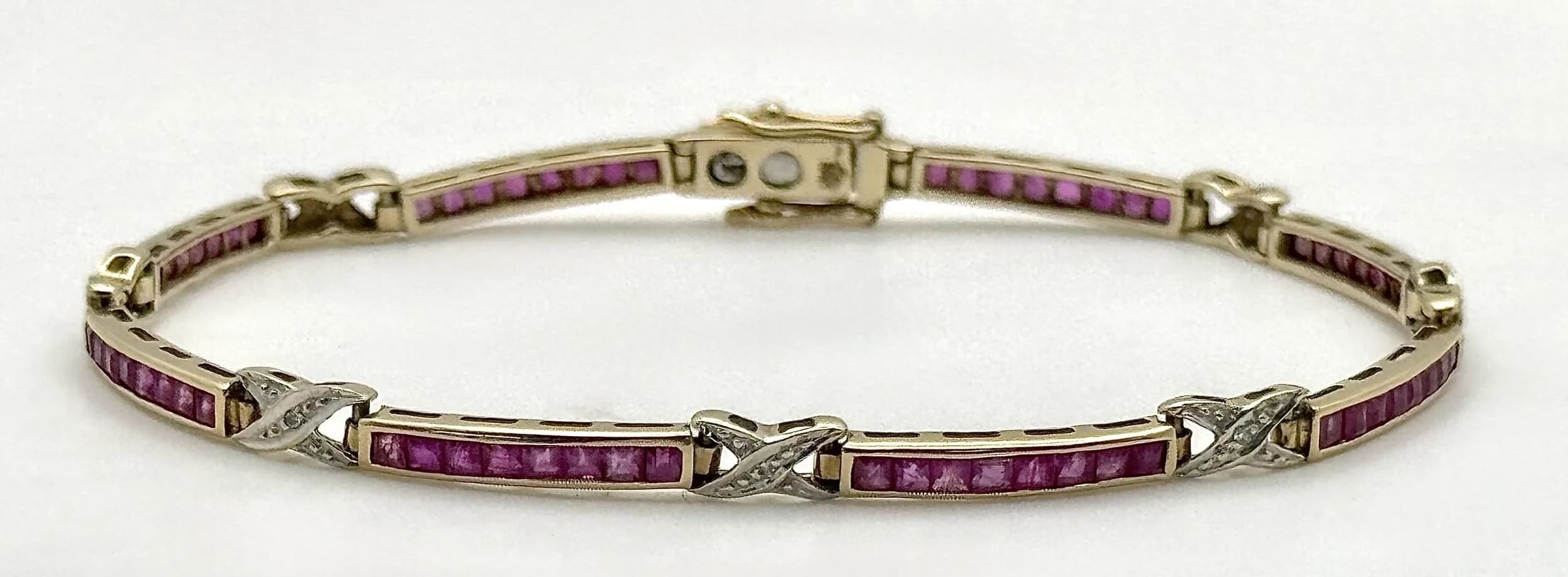 A 9K Gold Ruby Tennis Bracelet with Diamond Accents. Bar links of channel set rubies, with diamond accents in a lovers- cross form. 18cm. 5.9g total weight.