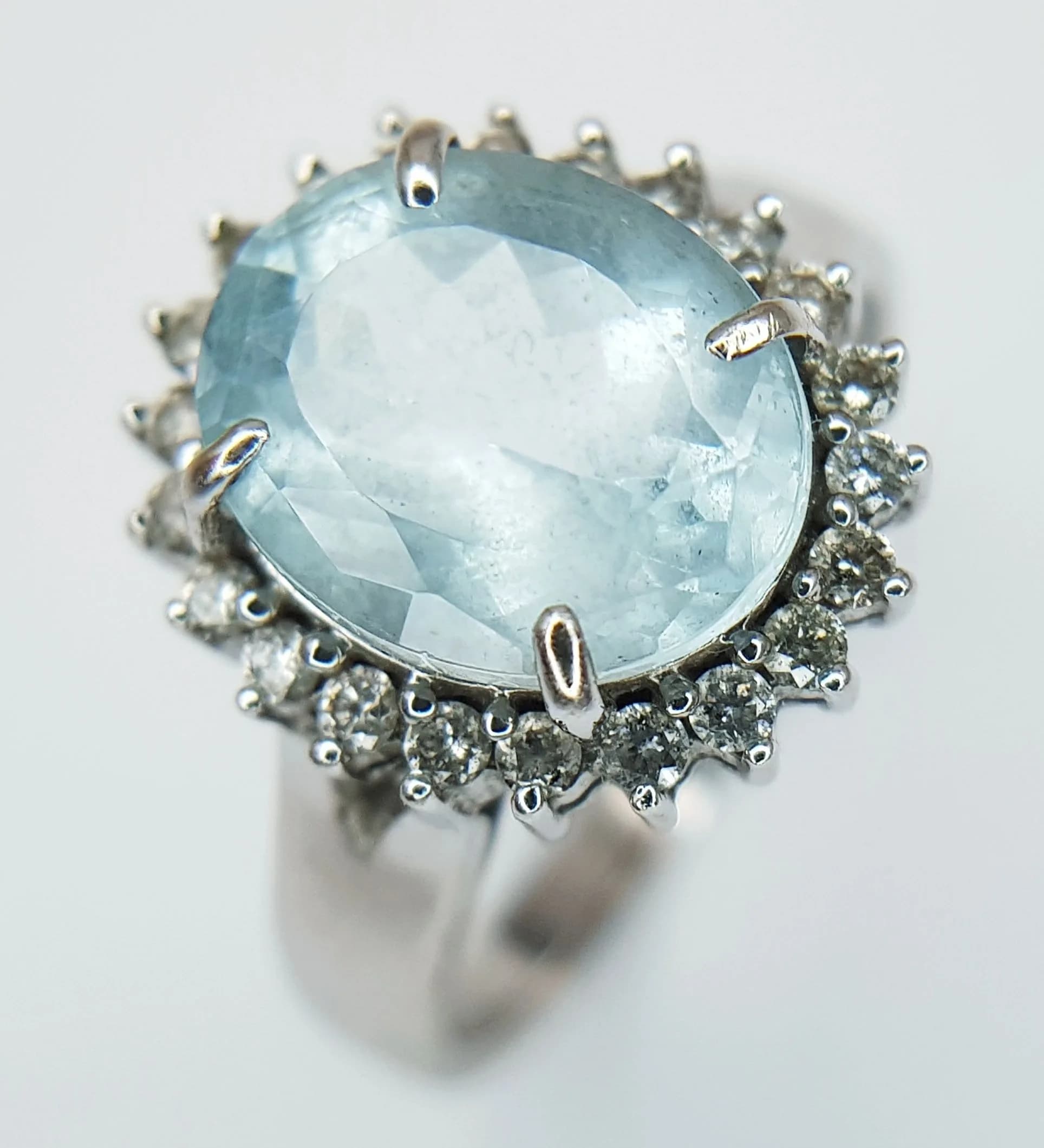 A 14K White Gold Aquamarine and Diamond Cocktail Ring. Circa 5ct oval cut aquamarine with a diamond surround of c. 0.60ctw having F colour with SI1/2 clarity. Size O. 4.9g.