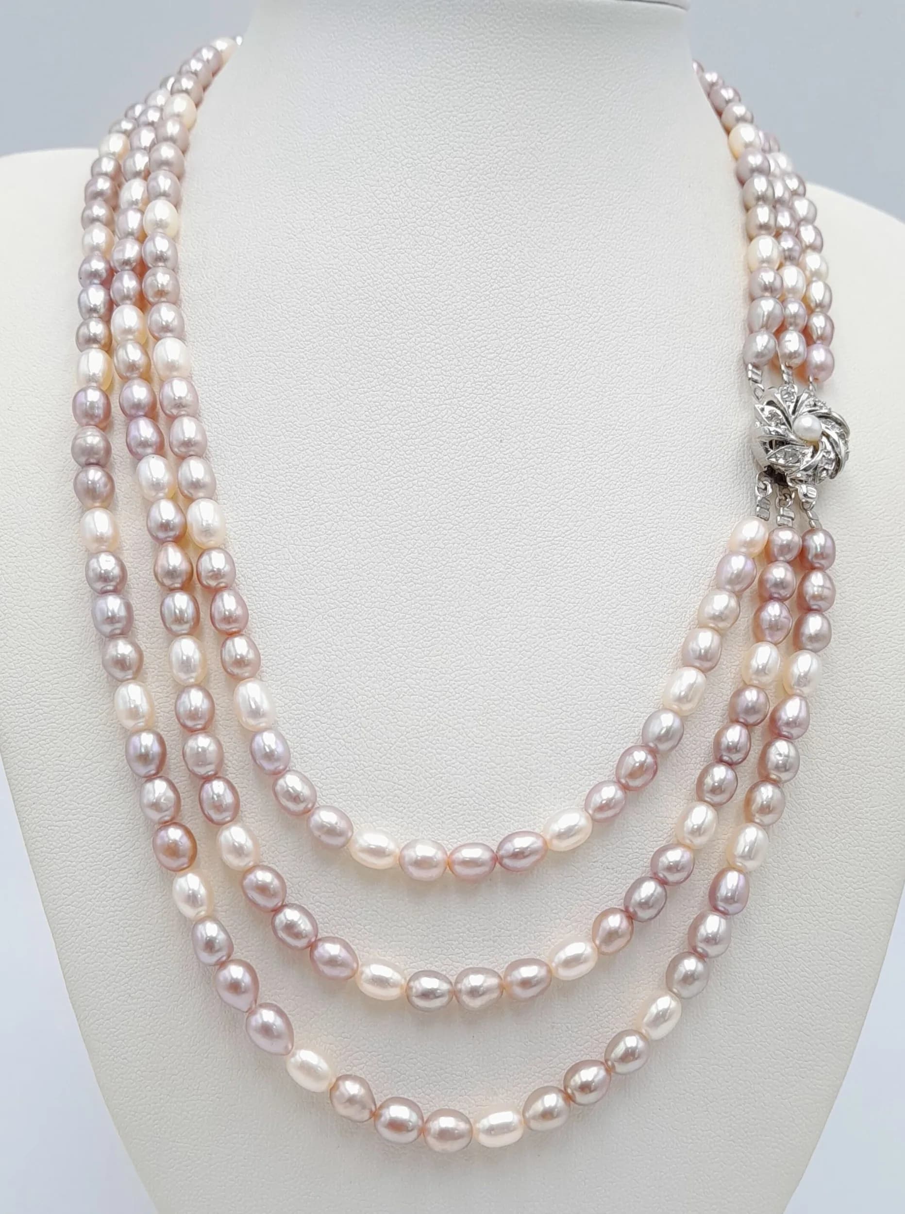 A magnificent Three Strand freshwater statement Pearl Necklace. In natural white, purple and pink tones, secured with a decorative floral clasp centred with a pearl and cluster white stones. Approximately 44cm in length. Please see photos or request a condition report.