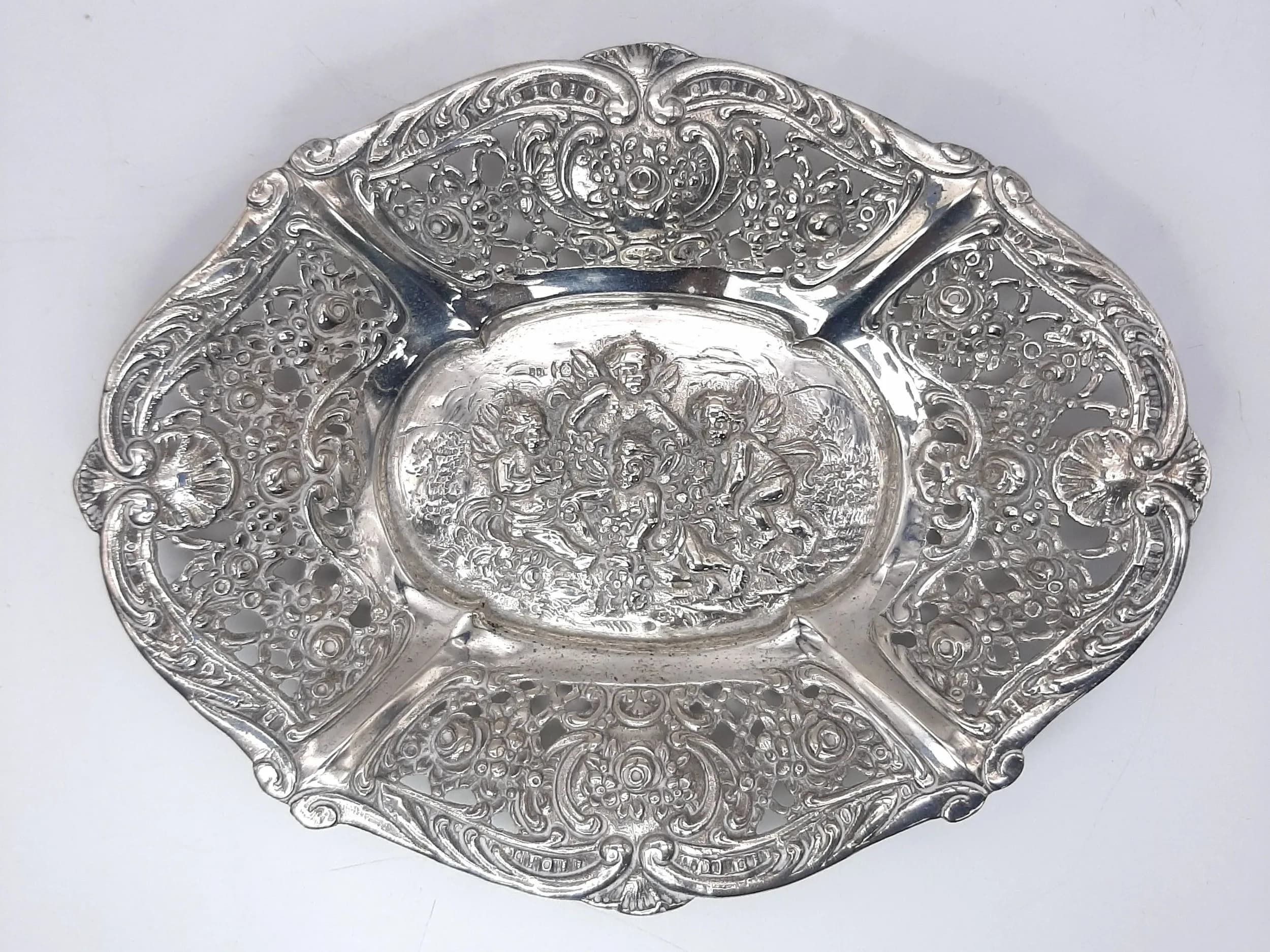 A Decorative Silver Candy Dish. Pierced and embossed floral border with a central cherub scene. Unhallmarked. Total weight 58.35 grams.