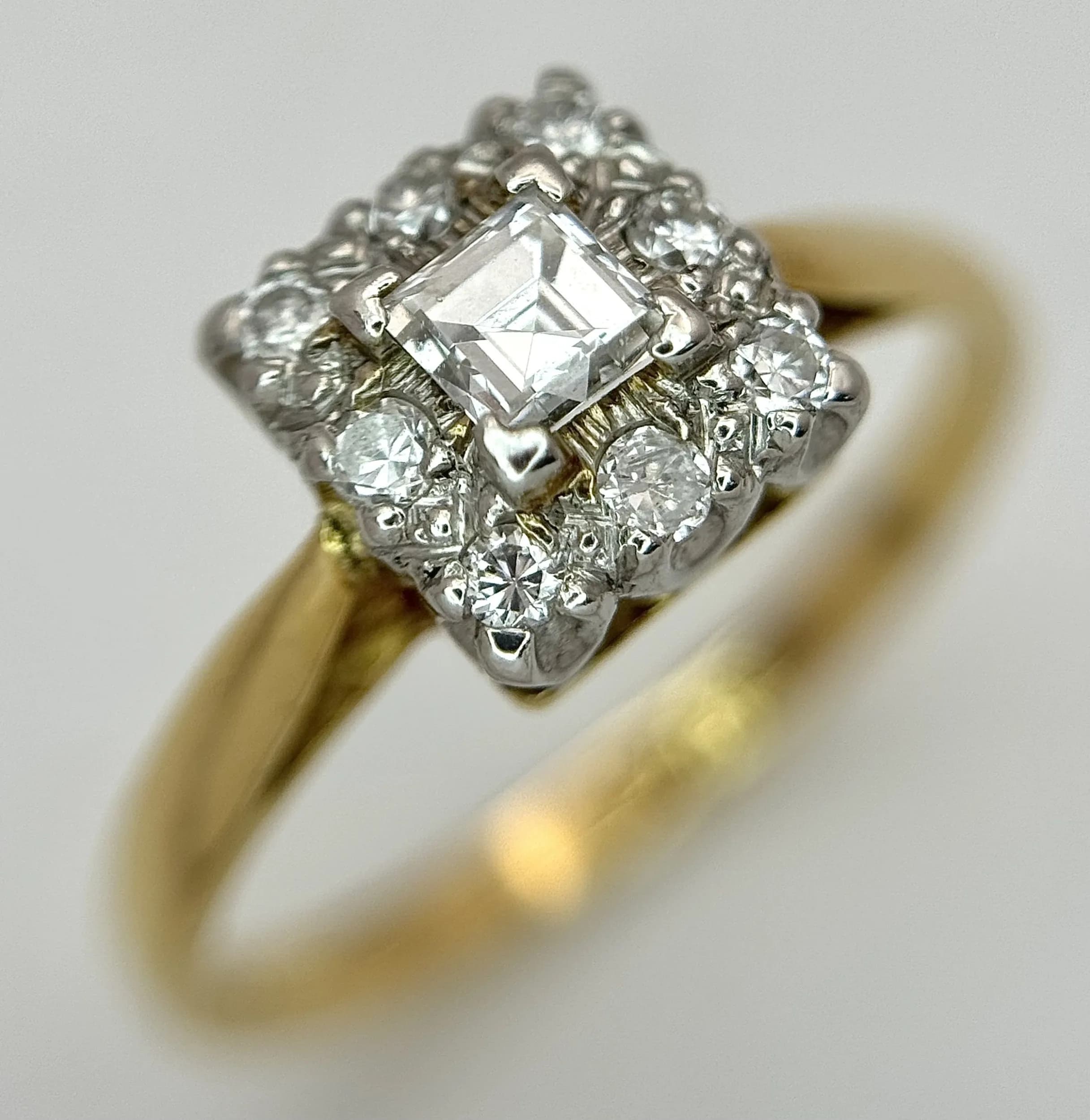 An 18K Yellow Gold and Platinum Diamond Cluster Ring. A 0.20ct Princess cut diamond with round brilliant cut diamond surround. Circa 0.50ctw diamonds having G-H colour and SI1/2 clarity. Size M. 2.7g total weight.