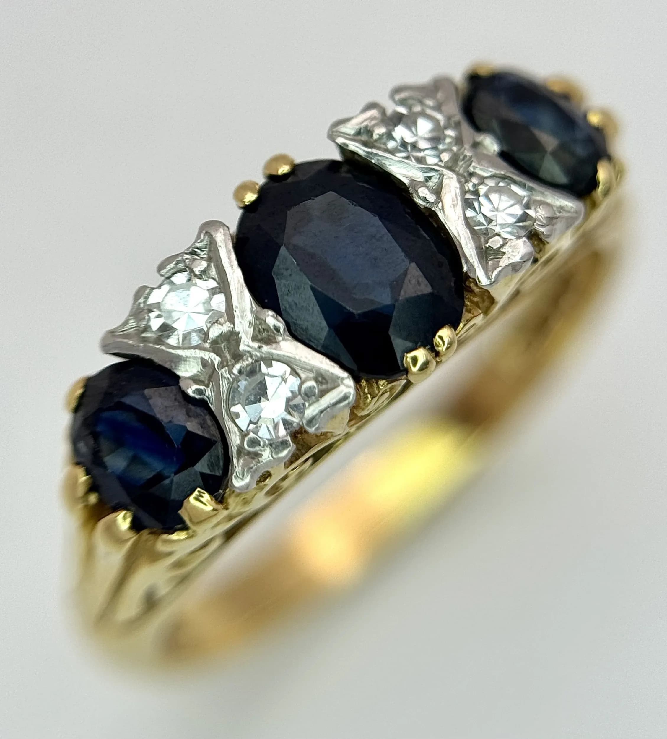 An 18K Yellow Gold, Diamond and Sapphire Ring. Three oval cut sapphires 0f 1ctw with diamond accents. Size L 1/2. 4.8g total weight.