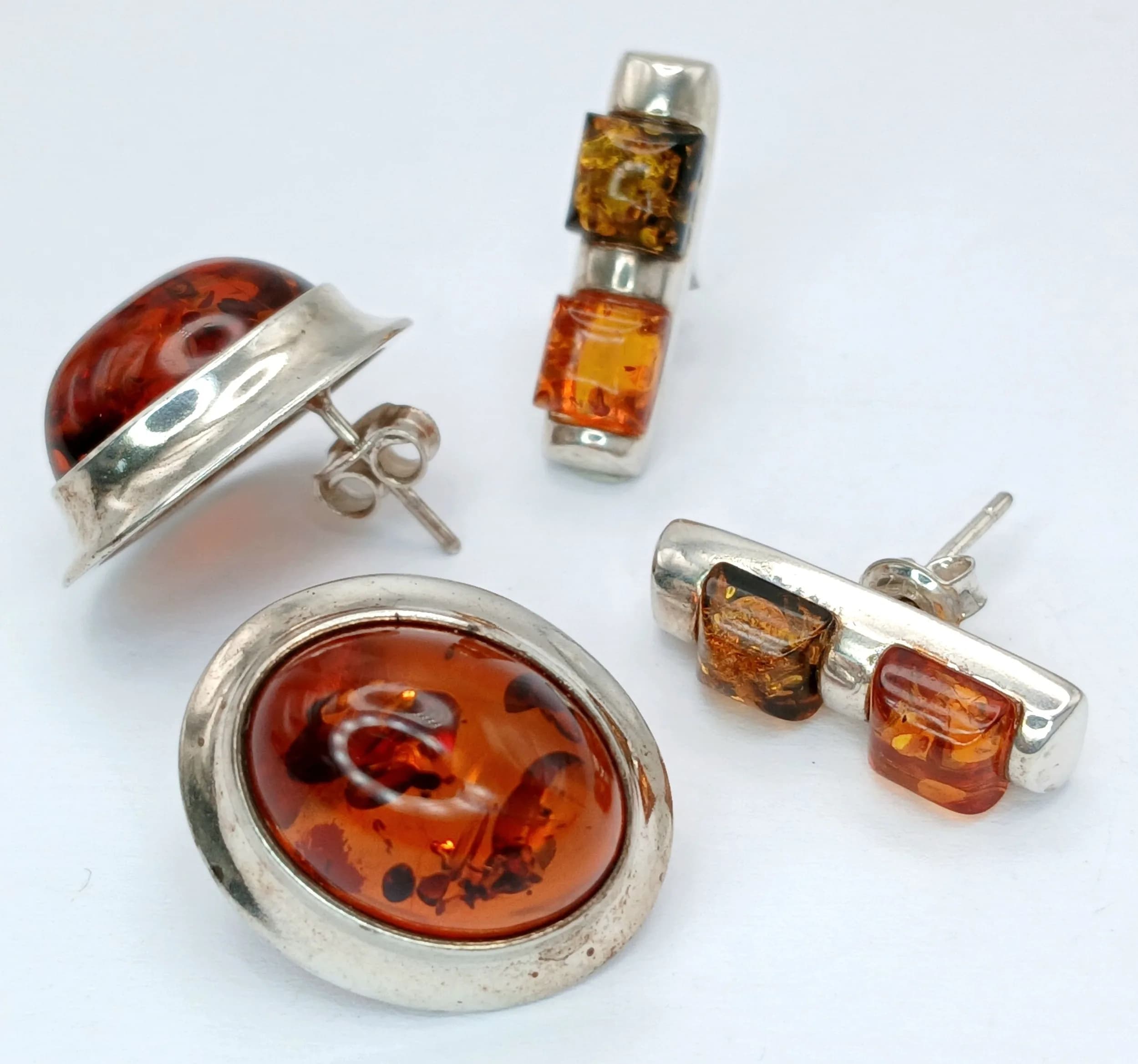Two Pairs of Sterling Silver Amber Earrings. Comprising 1) A 2cm Length Pair of Amber Cabochon Stud Earrings and 2) A 2cm Length Pair of Orange Cognac and Green Amber Stud Earrings.