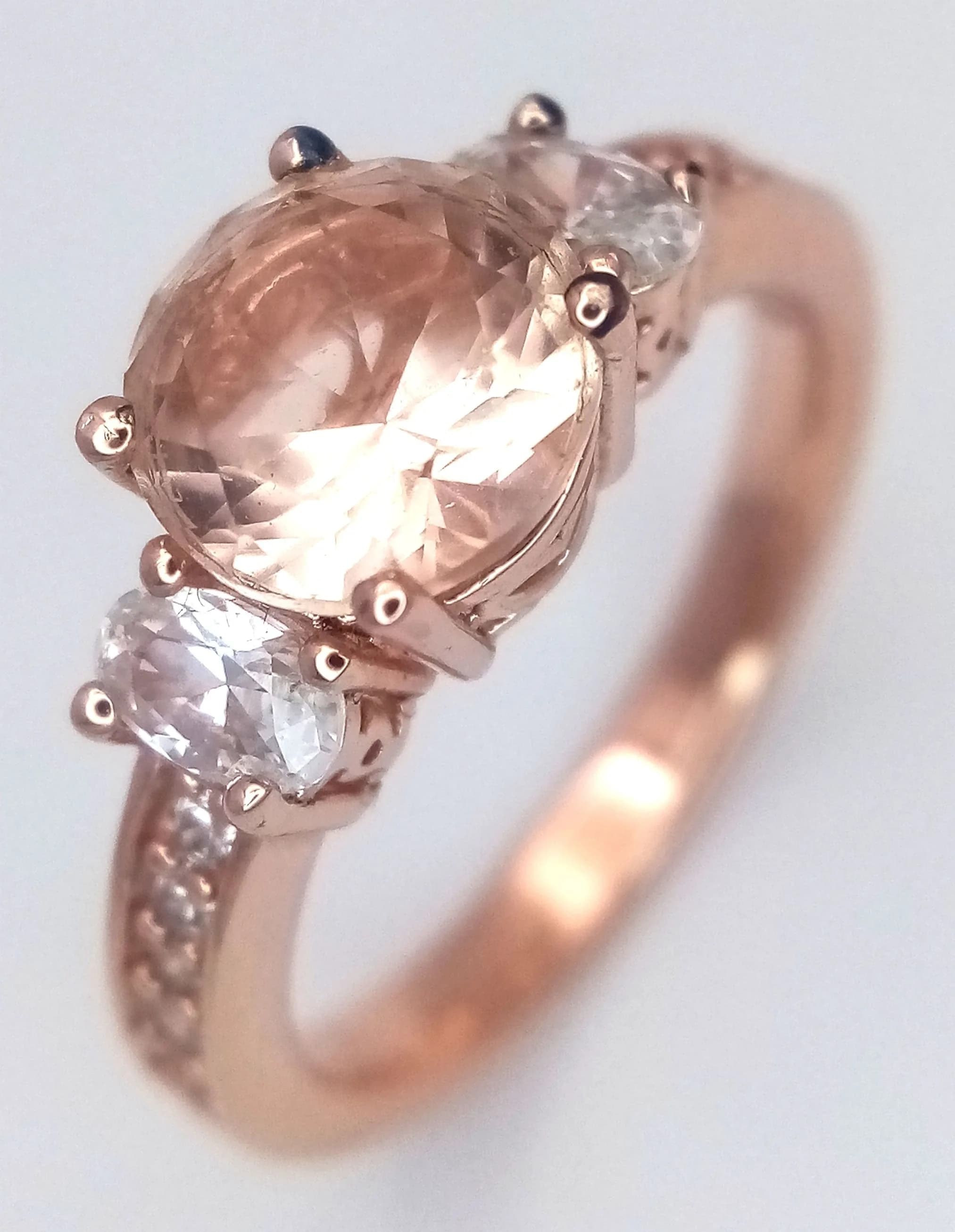 A Rose Gold Gilded Peach Pink and White Cubic Zirconia Ring Size P. The Ring is set with a centre 8mm Peach Pink CZ with further Oval and Round Cut CZ to the sides and upper shank. Gross weight 4.12 grams.