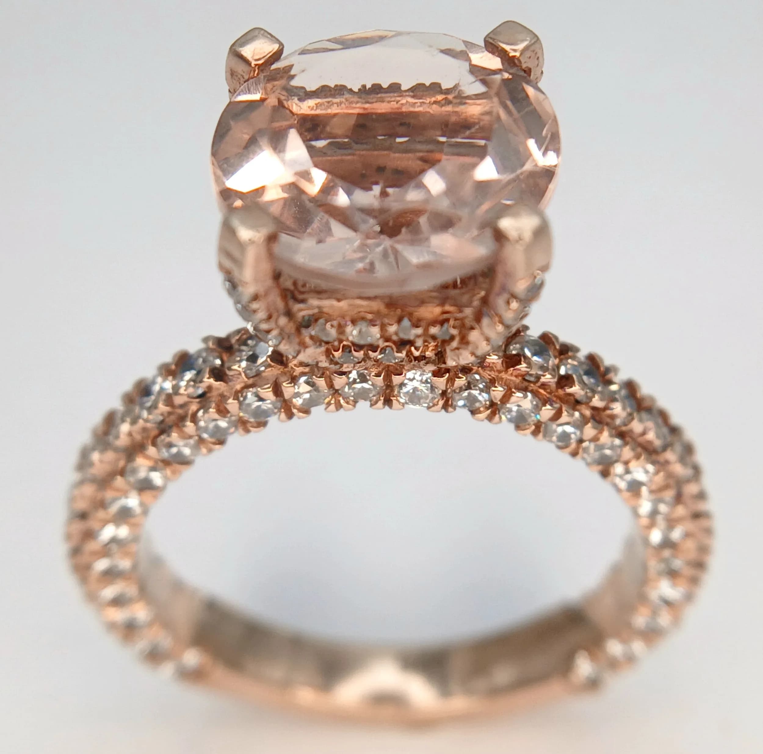A Rose Gold Gilded Sterling Silver High Mount Peach Pink and White Cubic Zirconia Set Ring Size O. The Ring is set with a 1cm Round Cut Peach Pink Cubic Zirconia with a profusion of round cut Cubic Zirconia set into the mount and upper half of the shank. The Ring has a gross weight of 4.75 grams.