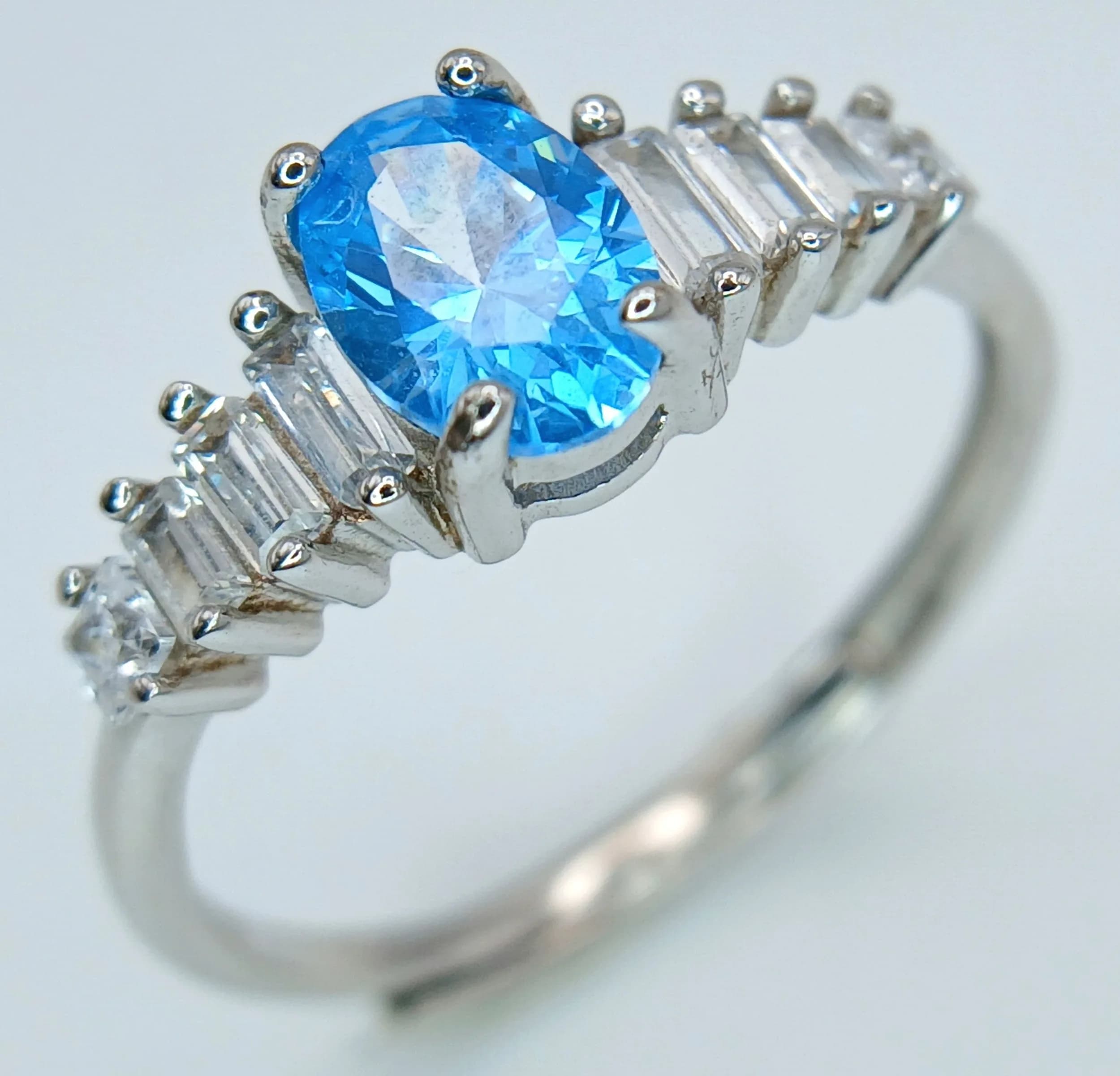 A Sterling Silver Adjustable Size Blue and White Stone Set Ring. Currently set at a size O. The Ring has the concealed overlap design shank that allows the ring to be adjusted in size. The Centre stone measures 7mm Length with the ring weighing 1.83 grams.