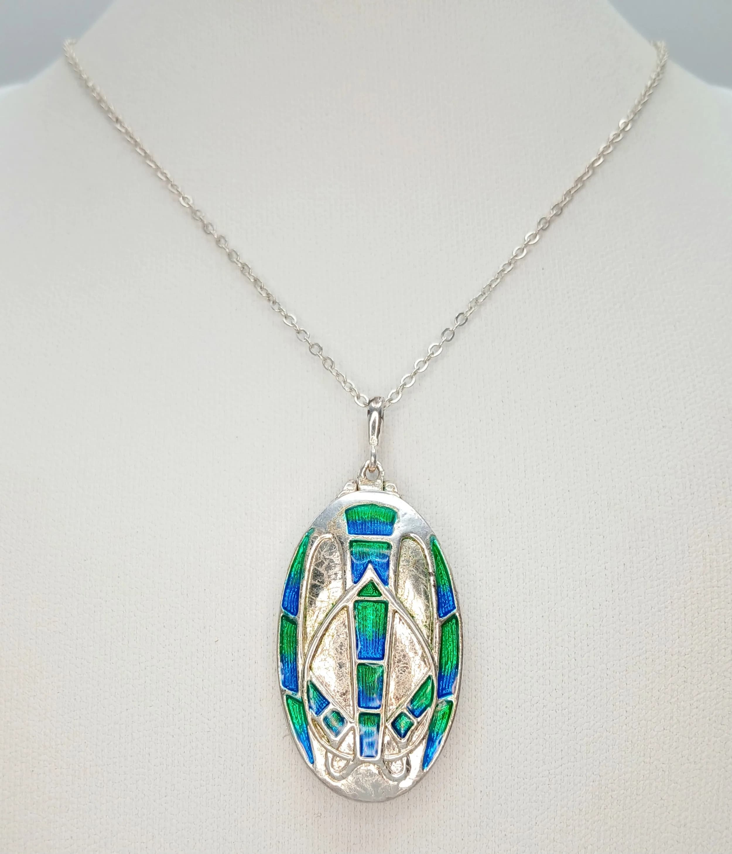 A Striking 925 Sterling Silver Enamel Locket Pendant Necklace – 62cm Length. The oval locket is decorated with blue and green enamel geometric detailing. The pendant measures 3.5cm x 2cm. Gross weight 15.48 grams.