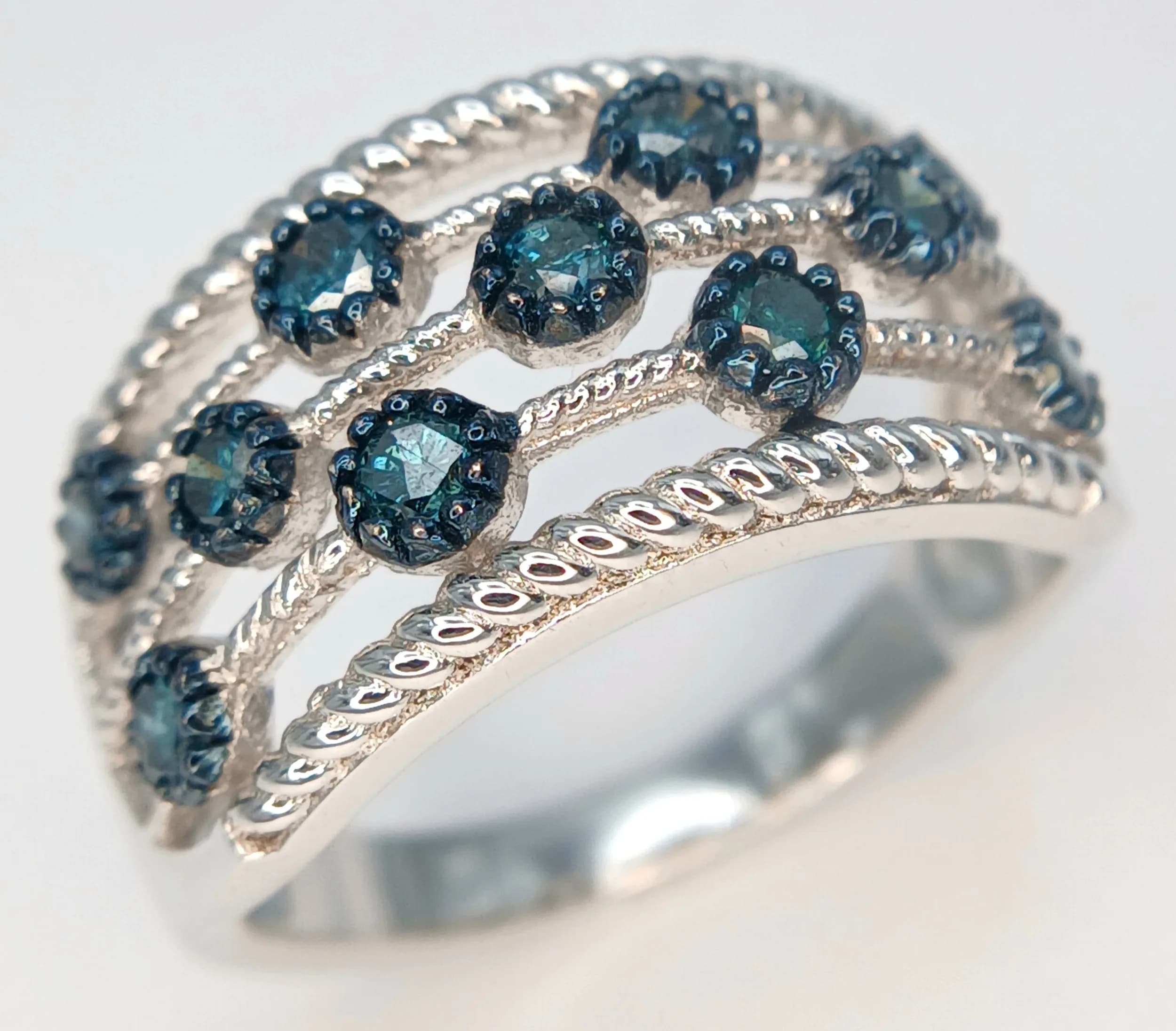 A Stylish Sterling Silver Blue Diamond Open Work Ring Size S. Set with round cut Blue Diamonds, approximately 0.20 carat. The Ring measures 1.2cm wide at the Crown and has a gross weight of 5.12 grams.