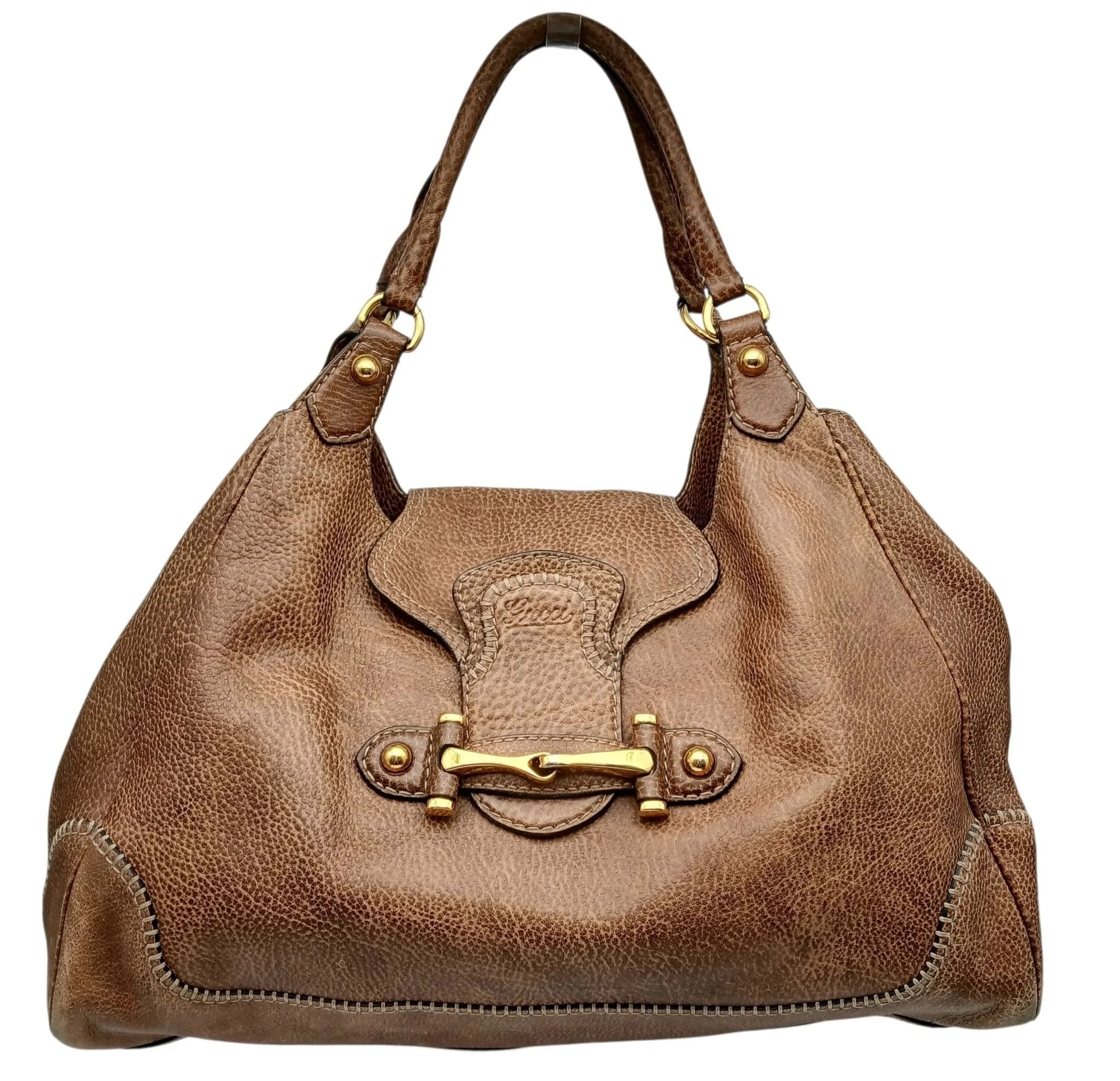 A Gucci New Pelham Large Hobo Shoulder Bag. Brown pebbled leather exterior with gold-tone hardware, signature horsebit detail to the front, decorative contrast stitching, double leather shoulder handles and protective base studs. Open top with a leather tab closure. Dark brown textile interior with one main compartment and a zipped inner side pocket. Approx. 42cm length x 30cm height x 18.5cm depth. Signs of wear to the corners and handles, a 1.5cm pen mark to the leather exterior and light stains to the interior. Please see photos or request a condition report. Ref: 29724.