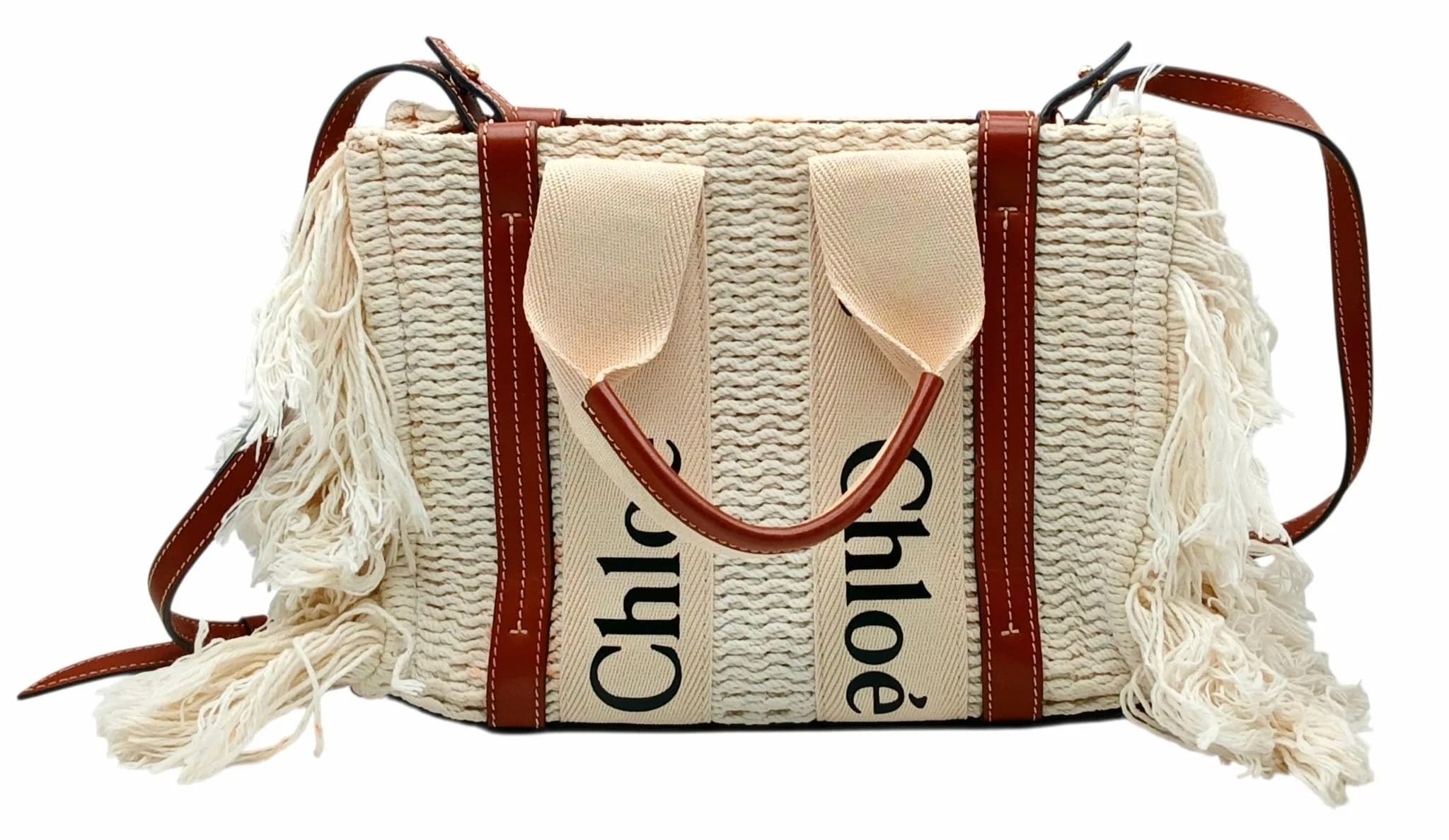 A Chloé Woody Fringed Tote Bag. Cream woven textile exterior with long fringed sides, tan leather trim, adjustable shoulder strap and Chloé logo canvas top handles. Open top opens to a grey textile interior with one main compartment and an open inner side pocket. Comes with a dust cover bag, authenticity card and original receipt. Approx. 28cm length x 20.5cm height. Some stains and signs of wear to the exterior - Please see photos or request a condition report. Ref: 29656.