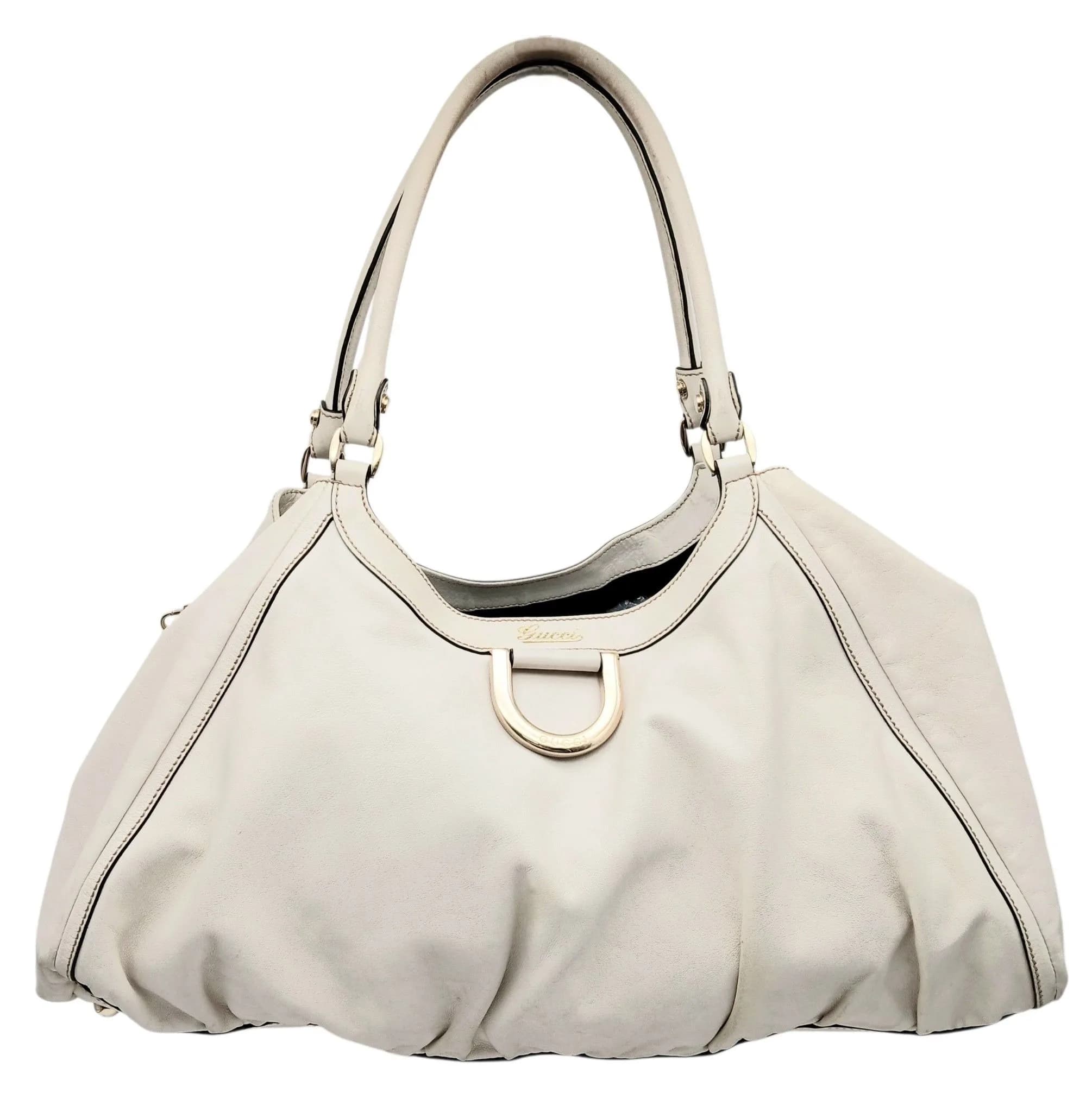 A Gucci Abbey D-Ring Shoulder Bag. Ivory white leather exterior with gold-tone hardware, signature D-ring detail and Gucci script logo to the front, double leather shoulder handles and protective base studs. Open top opens to a black textile interior with one main compartment, a zipped inner side pocket and an open inner side pocket. Comes with booklets. Approx. 44cm length x 27cm height x 21cm depth. Stains and marks to both exterior and interior - Please see photos or request a condition report. Ref: 29775.