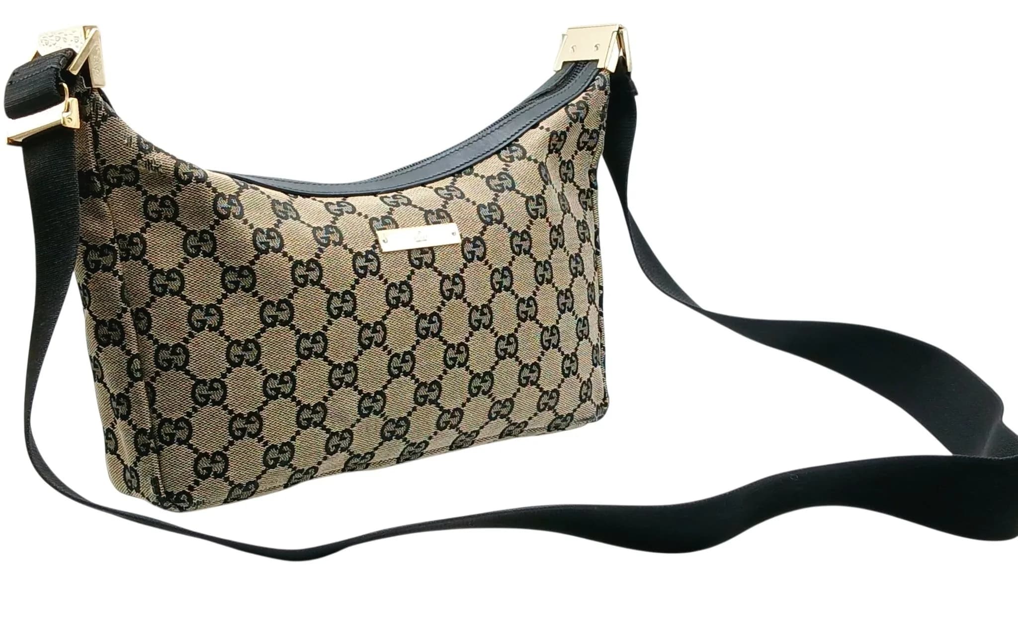 A Gucci GG Monogram Canvas Shoulder Bag. Beige and black GG monogram canvas exterior with black leather trim, gold-tone hardware and an adjustable black webbing shoulder strap. Zip-top closure with a Gucci logo plaque to the front. Black textile interior with one main compartment and a zipped inner side pocket. Approx. 26cm length x 19cm height x 4cm depth. Comes with a dust cover bag. Light signs of wear or discolouration to the exterior and corners - Please see photos or request a condition report. Ref: 29710.