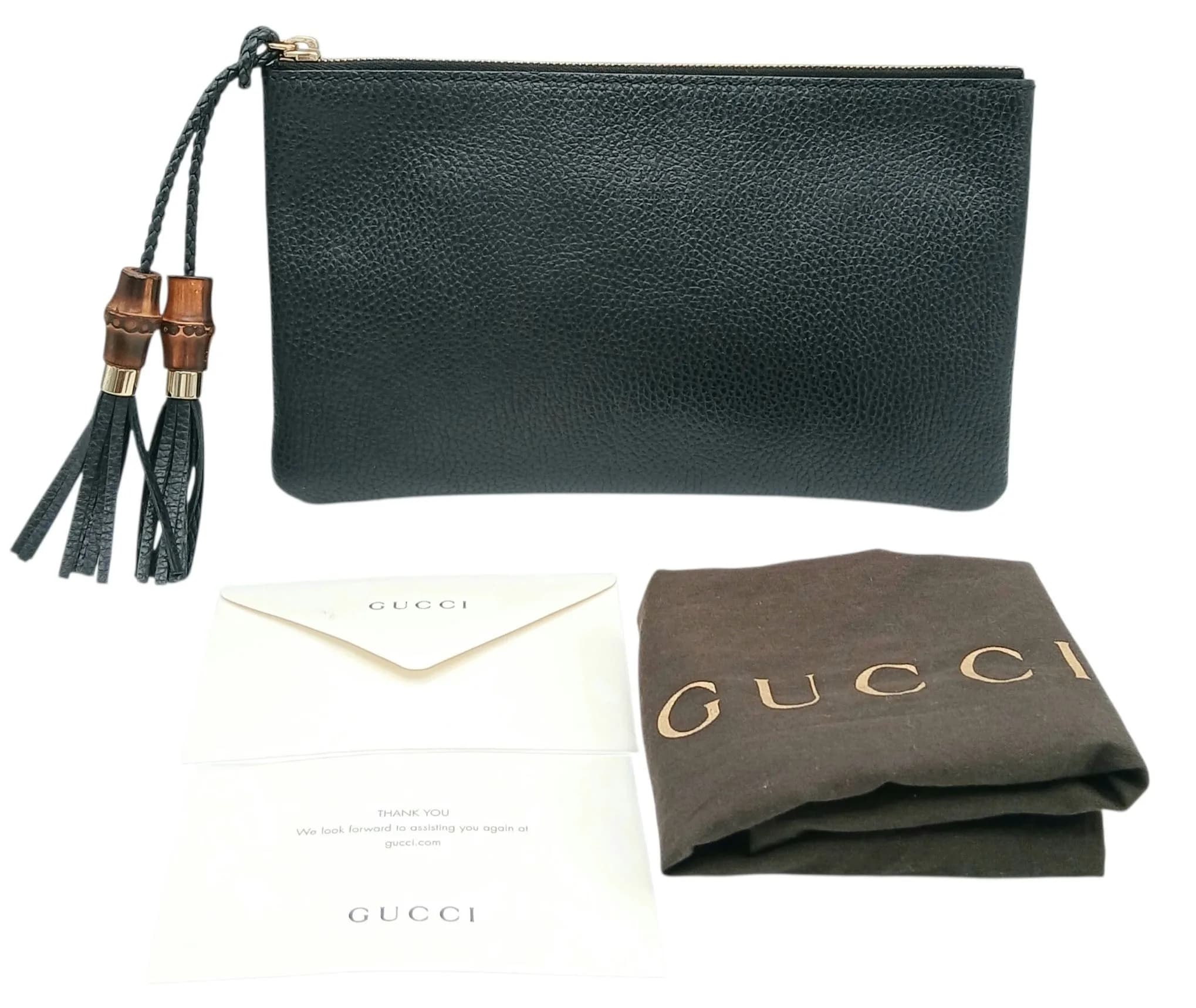 A Gucci Black Grained Leather Bamboo Tassel Clutch Bag. Black grained leather exterior with gold-tone hardware and signature bamboo and leather tassel zip pulls. Zip top closure opens to a black textile interior with one main compartment and an open inner side pocket. Approx. 25.8cm length x 15.5cm height. Comes with dust cover bag. In good overall condition but Please see photos or request a condition report. Ref: 29651.