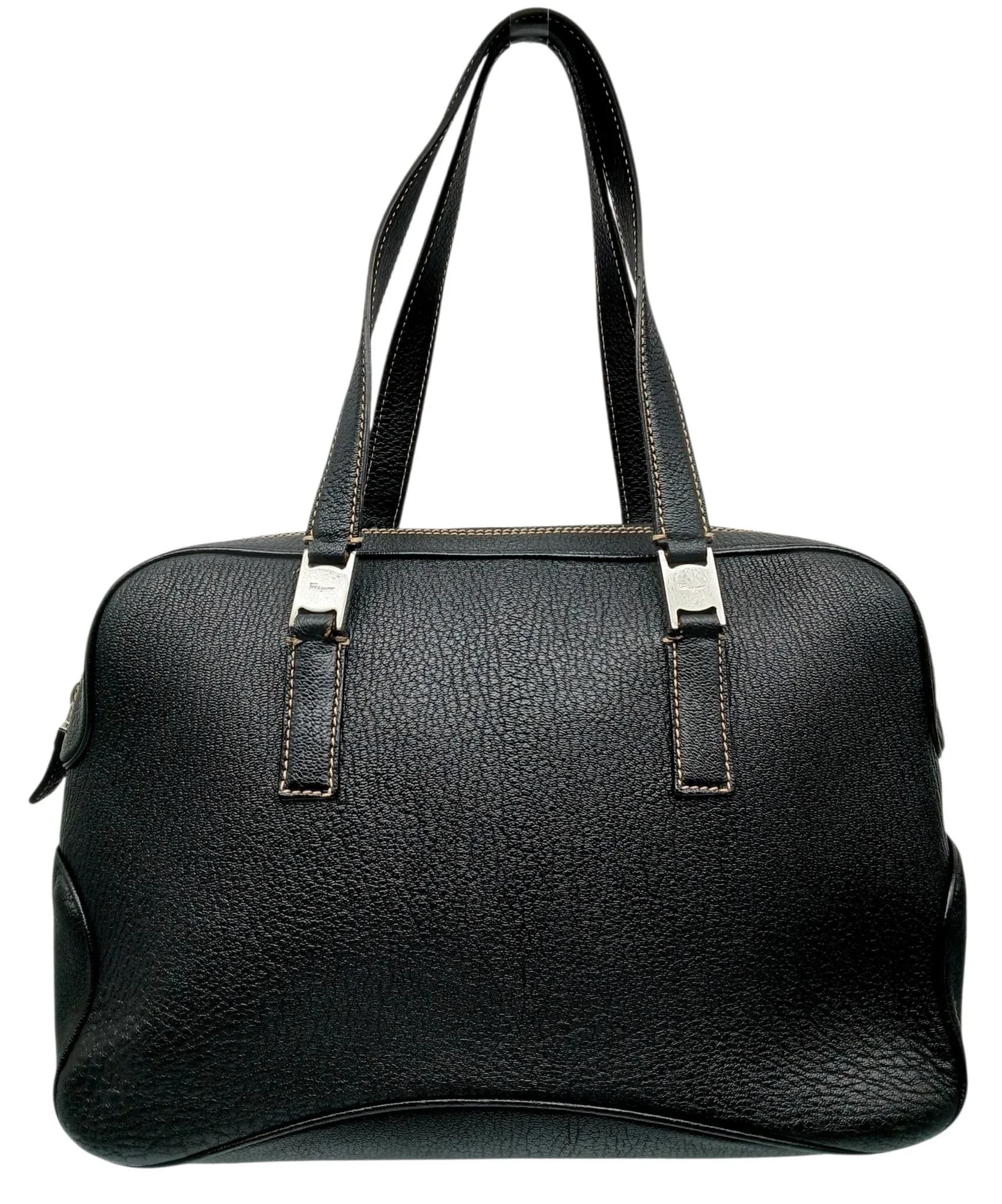 A Salvatore Ferragamo Black Leather Handbag. Black grained leather exterior with silver-tone hardware, contrast stitching, double leather shoulder handle, base studs and top zip closure. Opens to a beige suede interior with one main compartment, a zipped inner side pocket and two open inner side pockets. Comes with a dust cover bag. Approx. 34.5cm length x 23cm height x 11cm depth. In good condition overall but Please see photos or request a condition report. Ref: 29627.