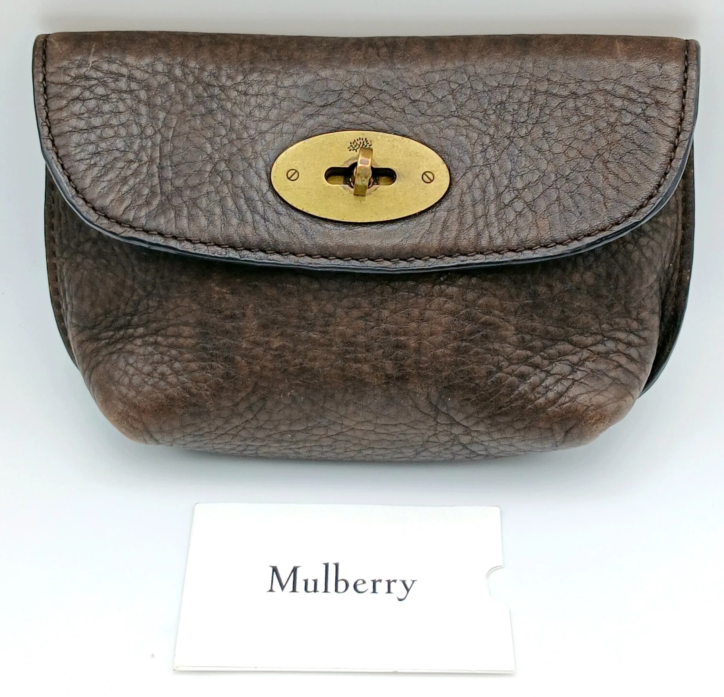 A Mulberry Brown Leather Clutch Bag. Dark brown grained leather exterior with brass-tone hardware and a front flap with oval turn-lock closure. Dark brown Mulberry logo-patterned textile interior with one main compartment. Comes with an original receipt. Approx. 21cm length x 13cm height. Light creasing and wear to the corners - Please see photos or request a condition report. Ref: 28563.