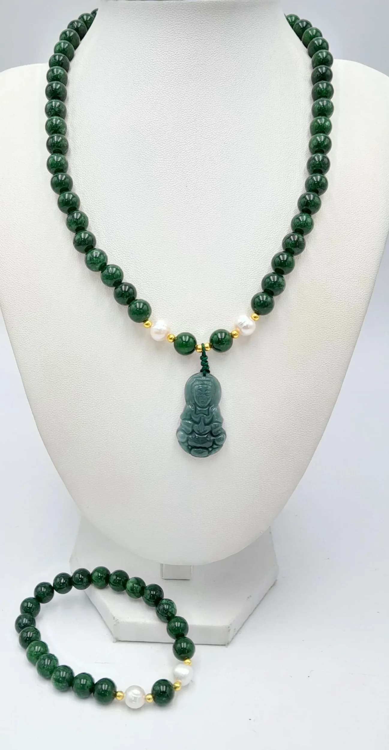 A Green Jade Carved Pendant Necklace with a Matching Bracelet. A polished green jade bead necklace with white pearls accent spacers, suspending a carved green jade buddha pendant. Together with a matching bracelet. Decorative gold gilded clasp. Necklace approx. 43cm length with a 4cm pendant drop. Please see photos or request a condition report.
