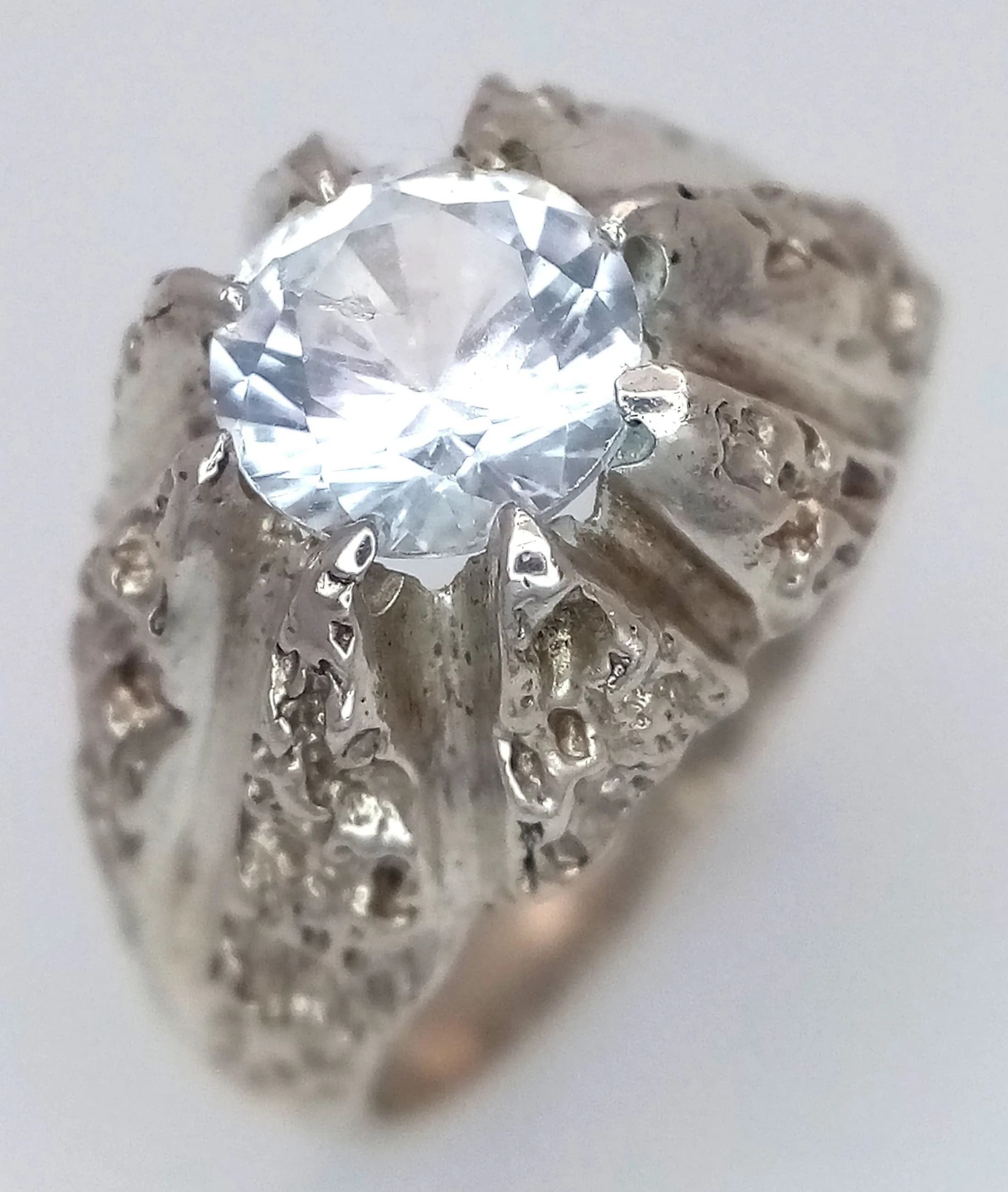 A Vintage Mid-Century, Sterling Silver Gypsy Style White Spinel Solitaire Ring Size N. Set with a 7mm Round Cut White Spinel, approximately 1.25 carat in a brutalist design mount. Gross weight 5.17 grams.